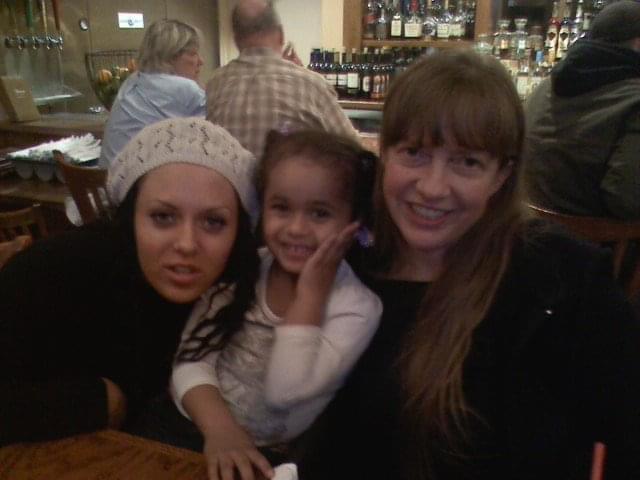 Two adults and a child smile while sitting at a table in a busy restaurant.