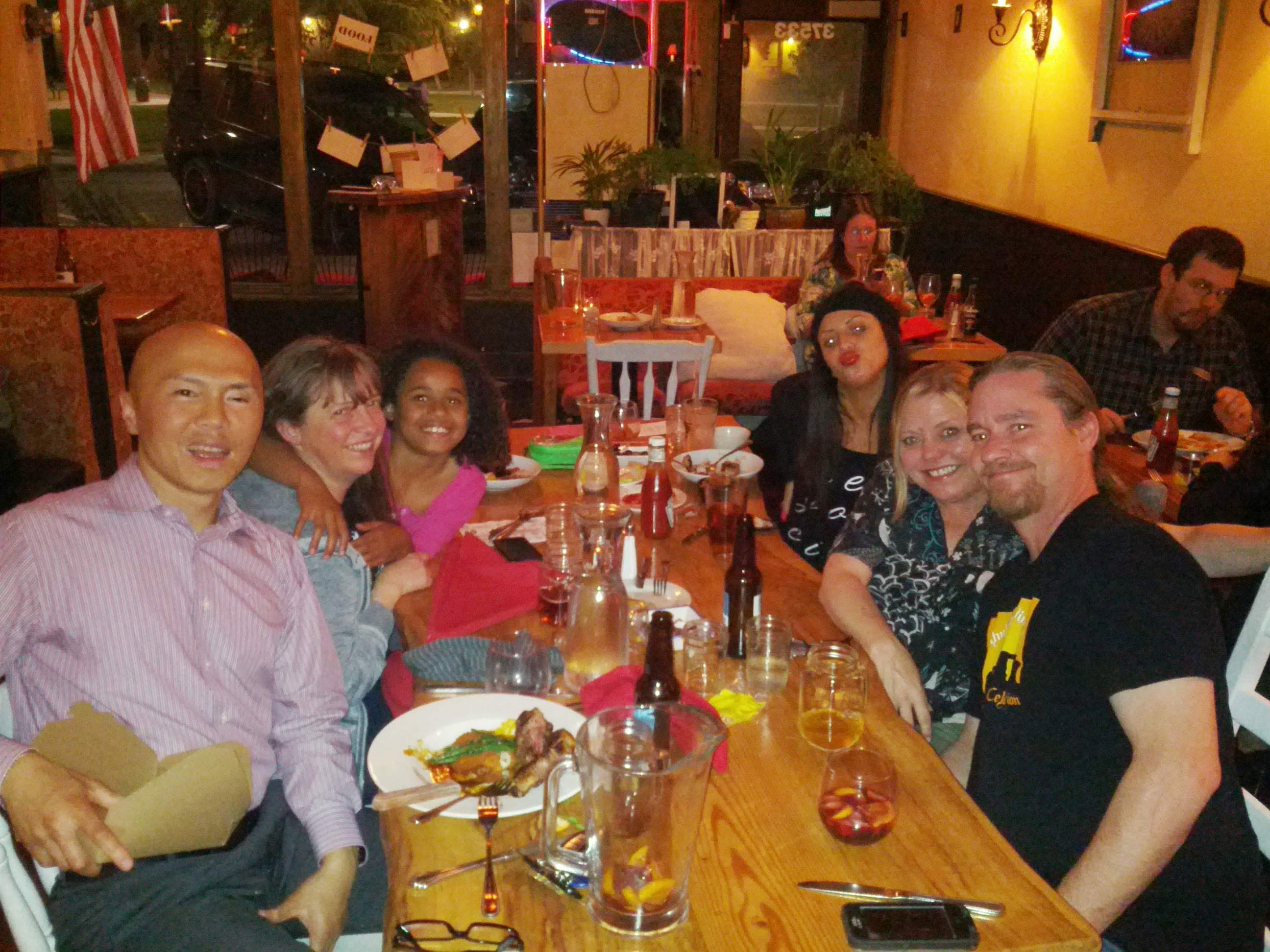 Several people gather around a table at a restaurant enjoying food and drinks in the evening.