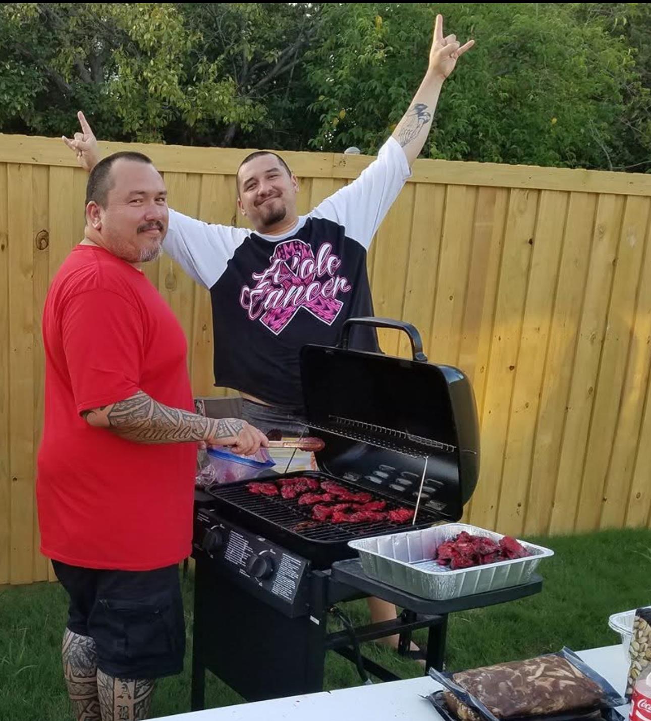 Two men prepare food on a grill in a backyard setting while enjoying their time together.
