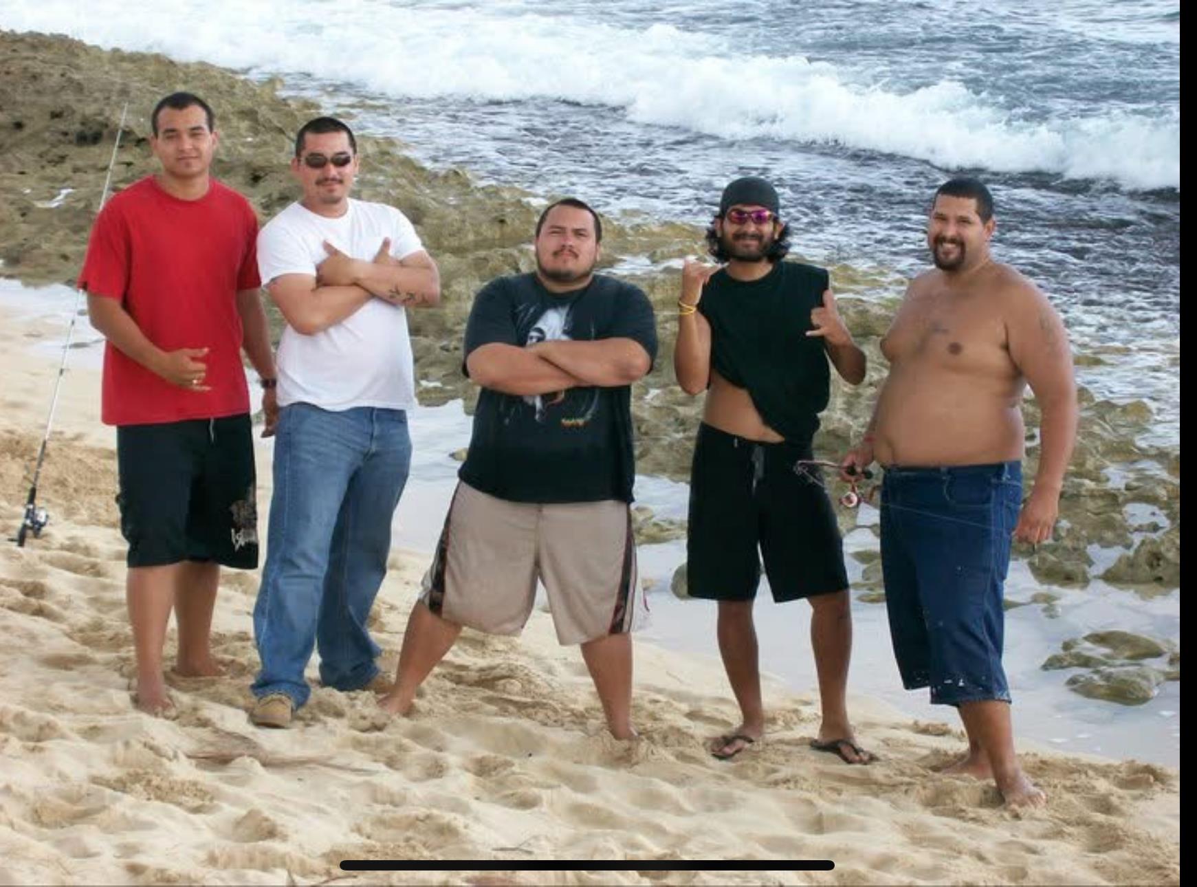Friends stand together on the sand by the water, enjoying a sunny day at the beach.