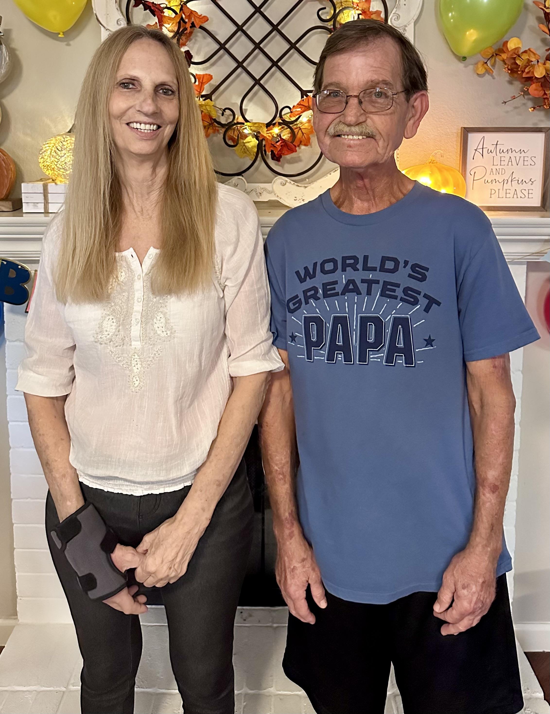 A man and woman smile standing in a cozy room with fall decorations.