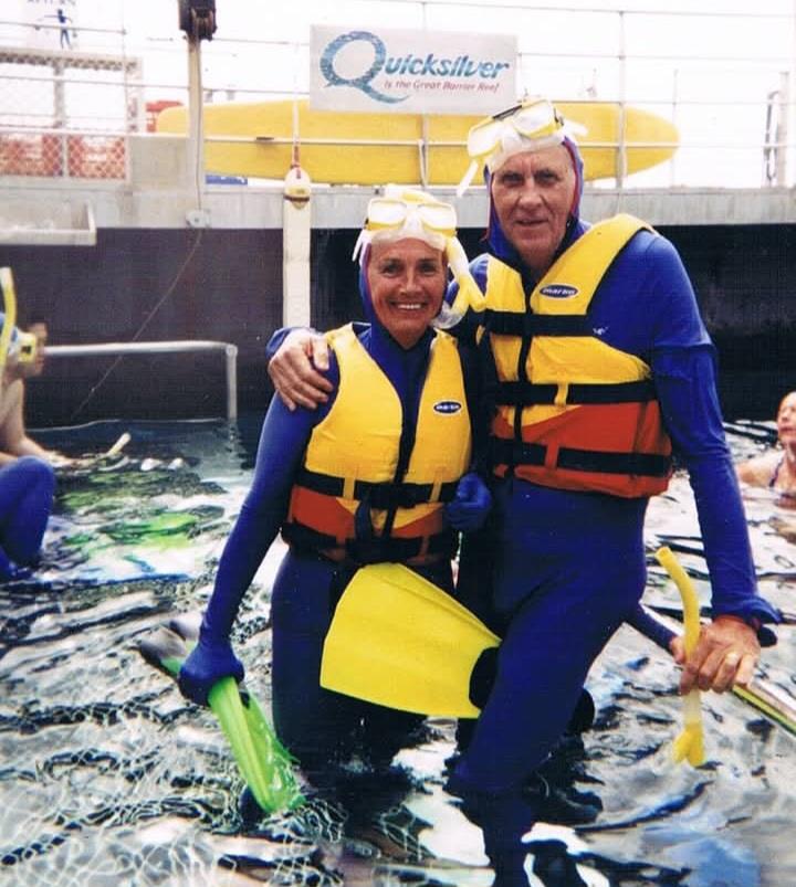 A couple wearing snorkeling gear stands in the water smiling while others swim nearby.