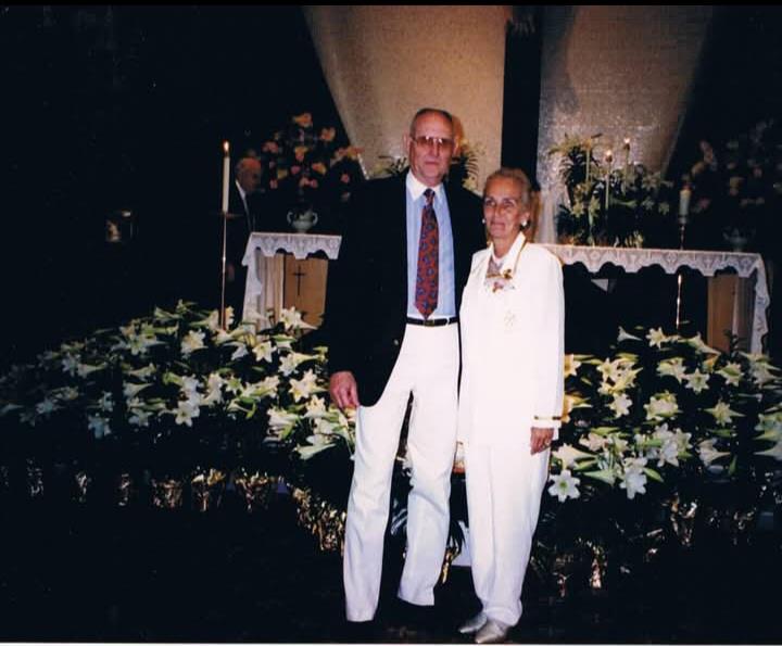 A couple poses for a picture in a church with flowers around them during a celebration.