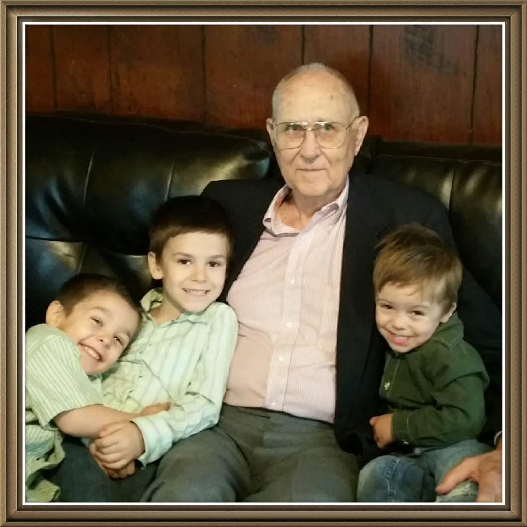 Three children sit on a couch with an elderly man who is smiling and spending time together.