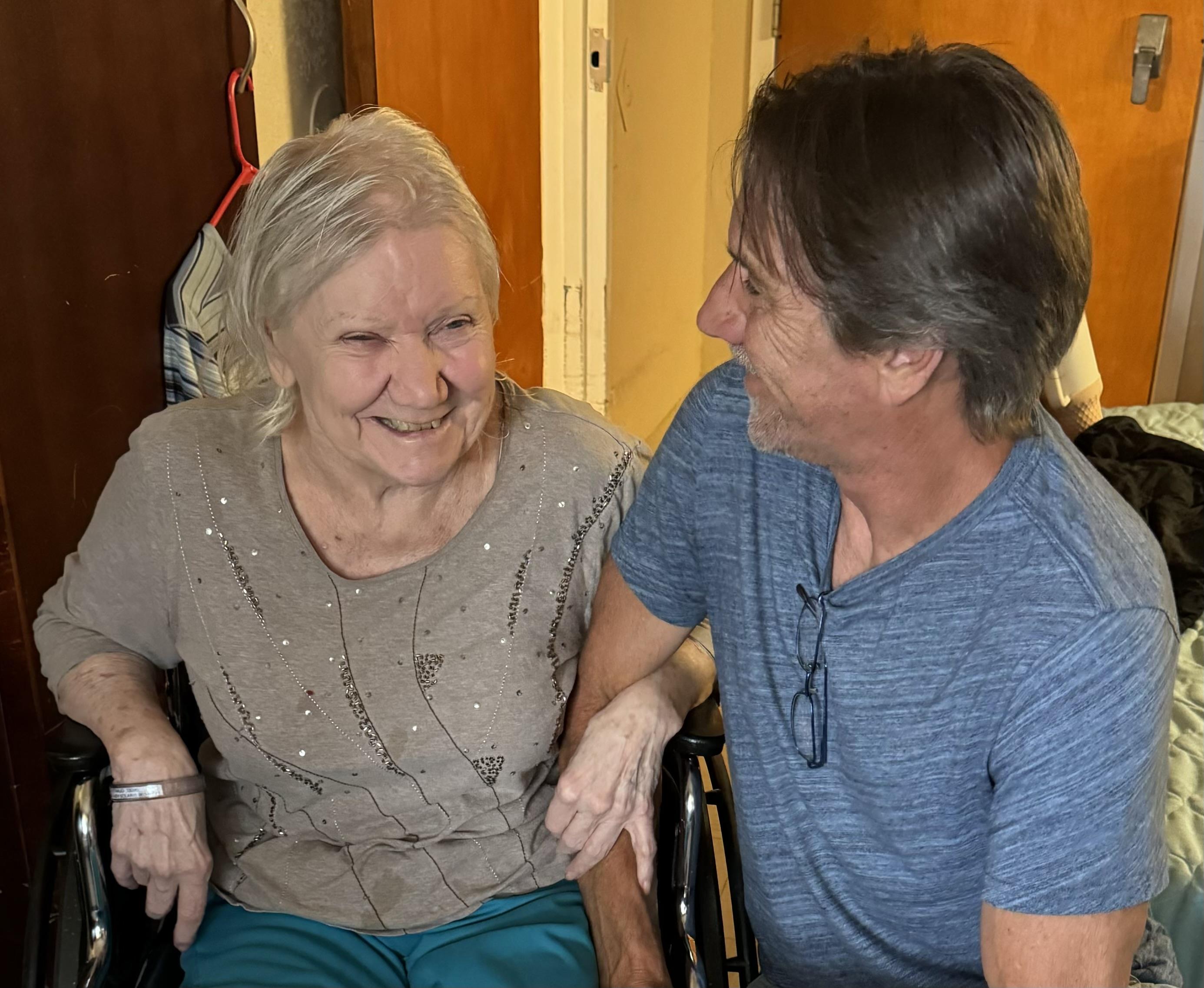 An elderly woman and a man have a joyful conversation at home during the day.