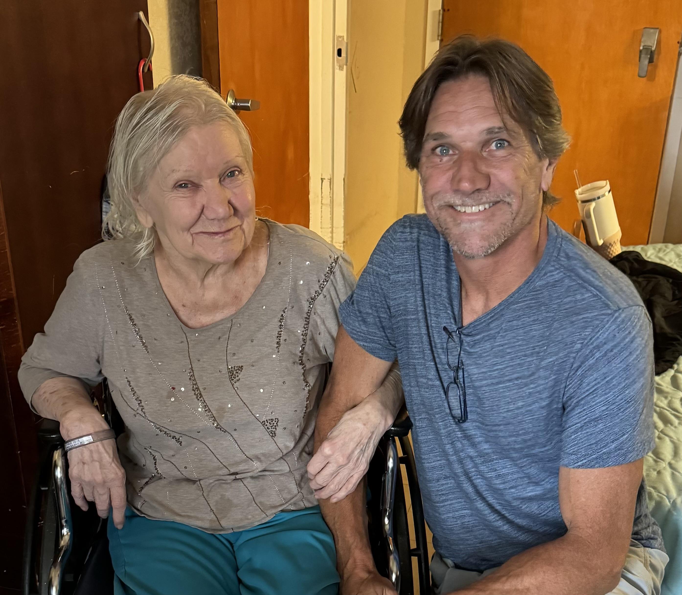 A man and an elderly woman sit together in a room during a visit in the afternoon.
