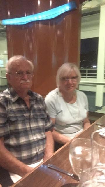 An elderly man and woman sit at a table in a restaurant at night. They look serious.