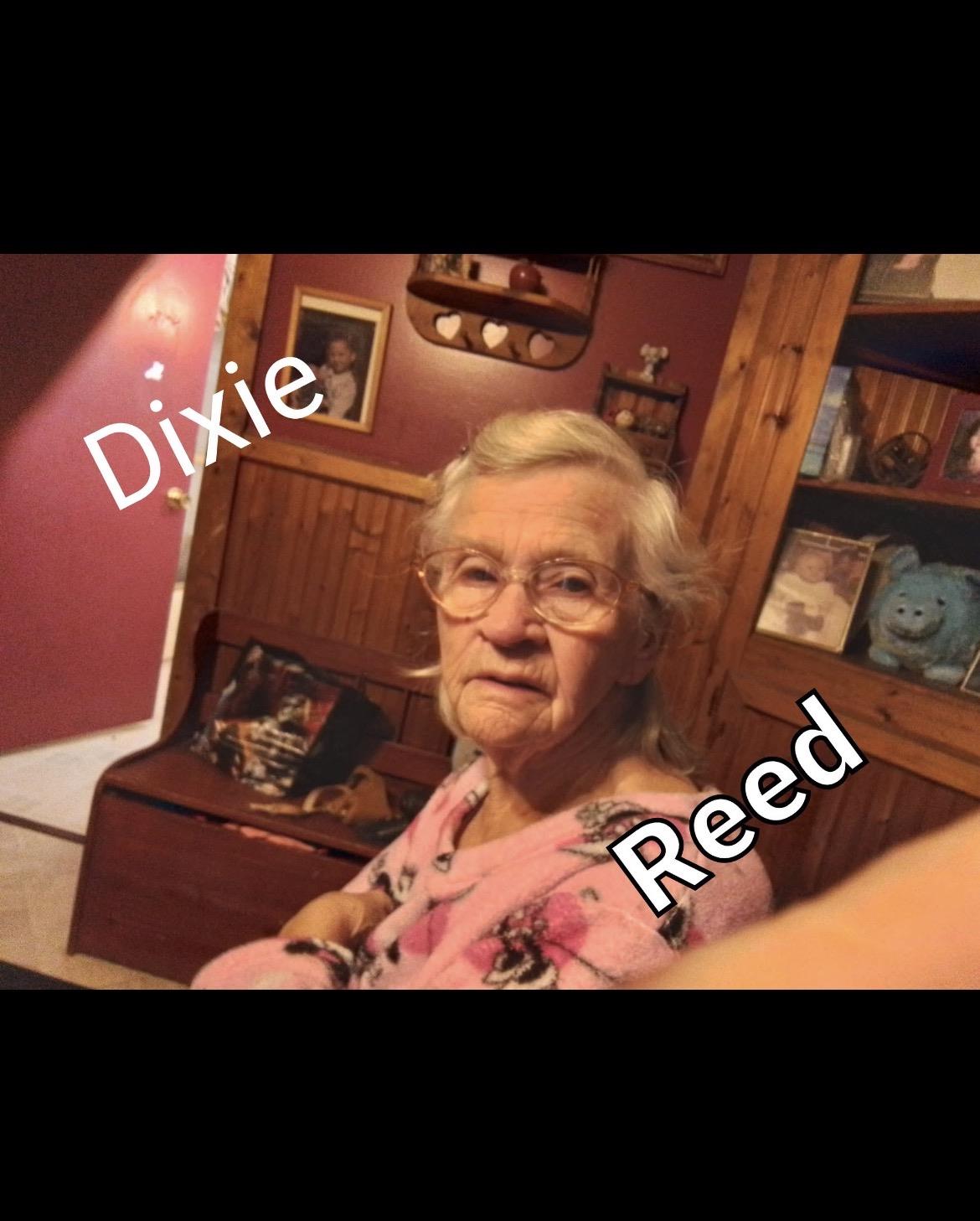 An older woman relaxes in her cozy room, surrounded by wood and personal items.