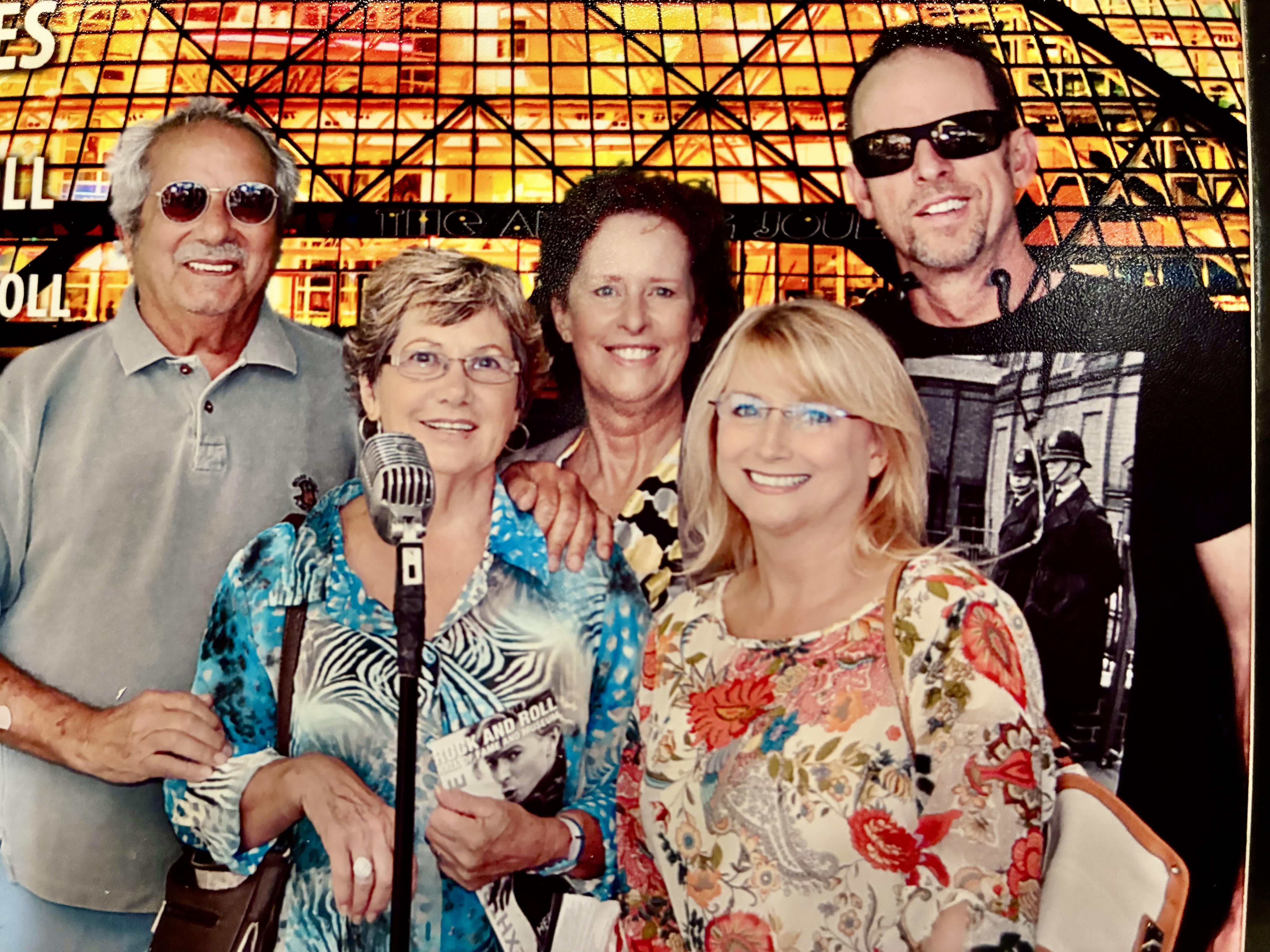 Five friends smile and pose for a picture at a venue with colorful lights behind them.