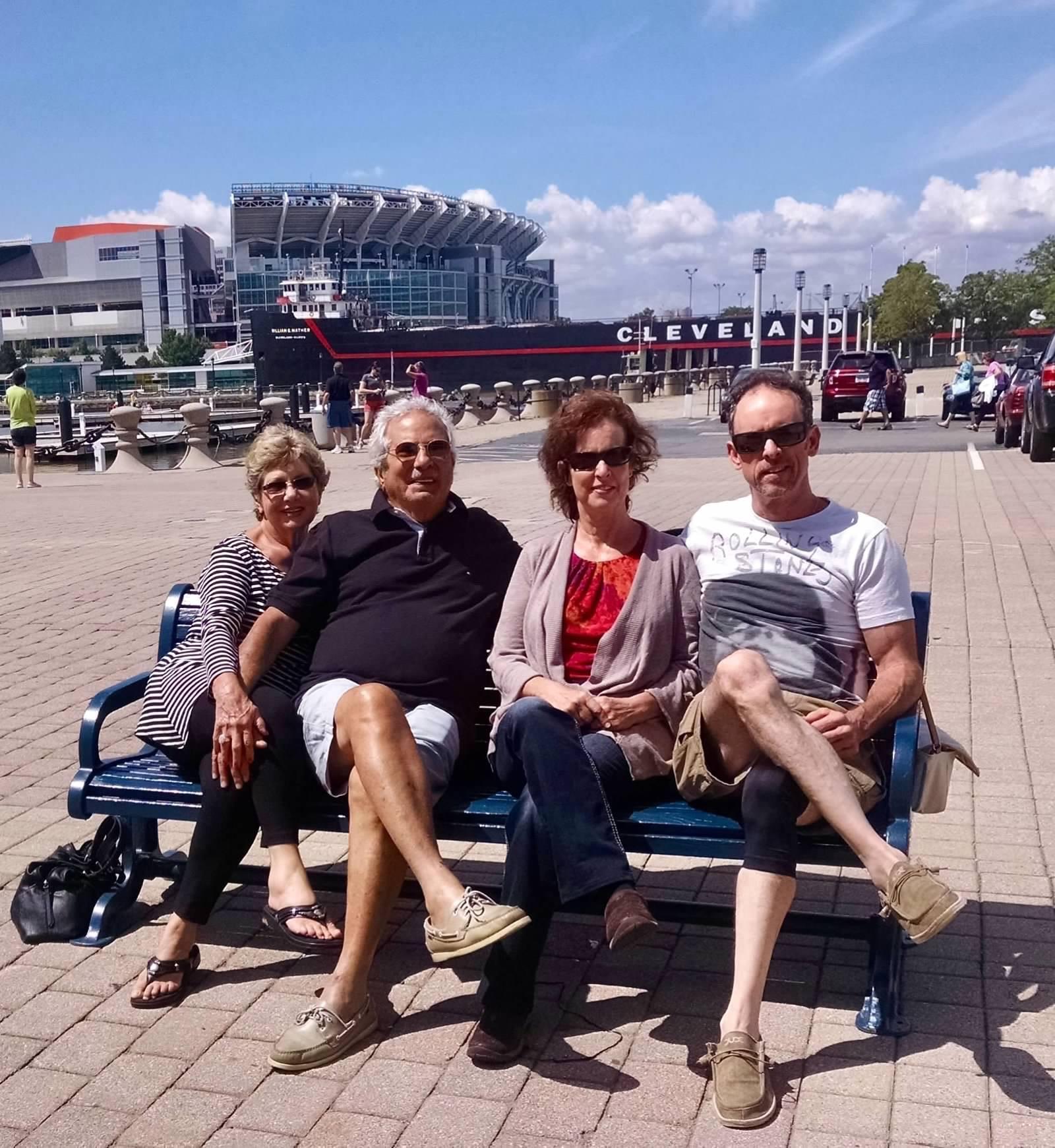 Four people relax on a bench by a stadium in Cleveland during a sunny afternoon.