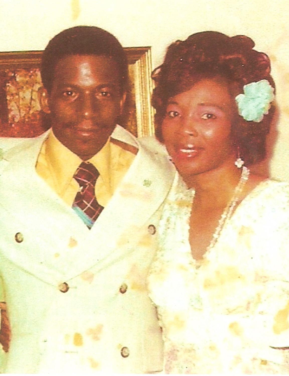 A couple poses closely together at a social event, wearing formal outfits and smiling happily.