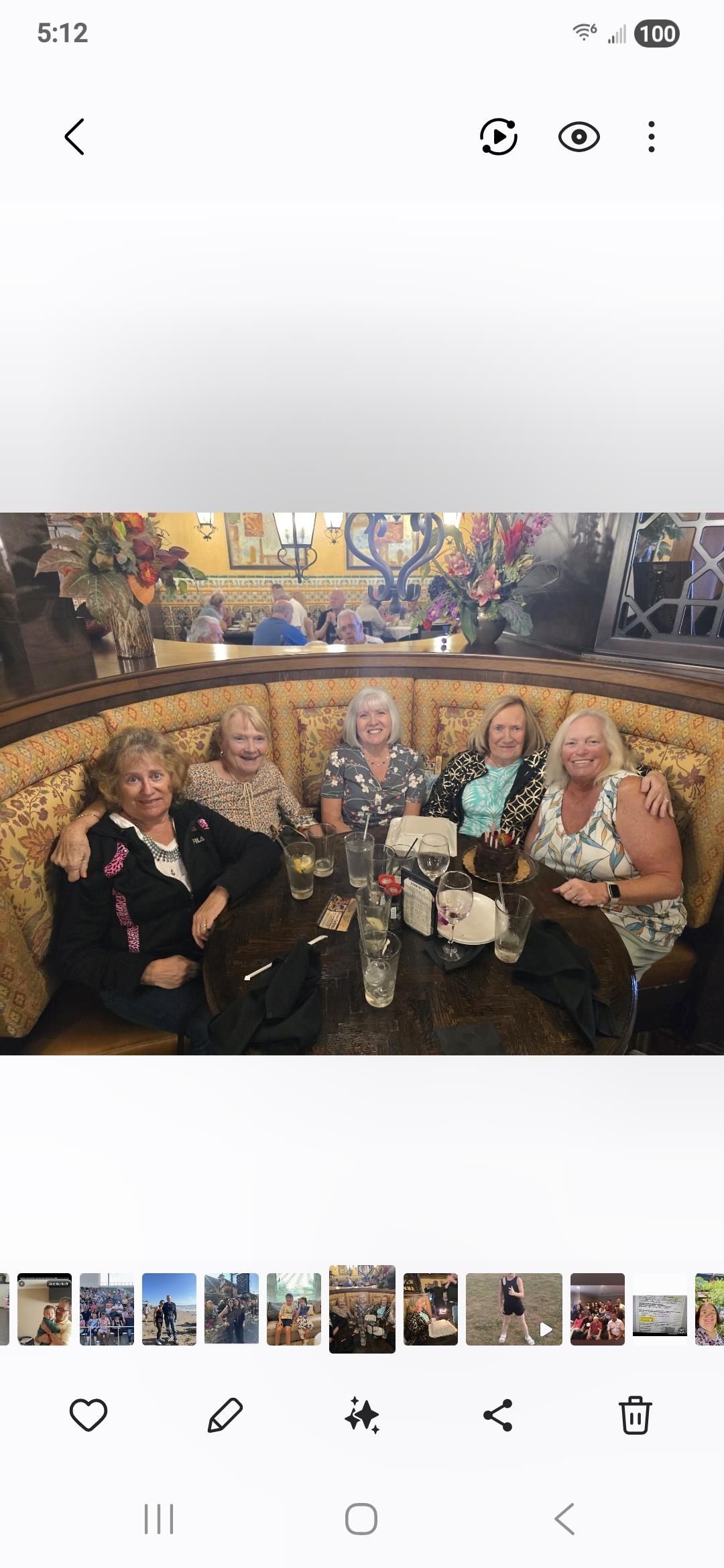 Five friends sit together at a restaurant booth sharing drinks and food while chatting and laughing.
