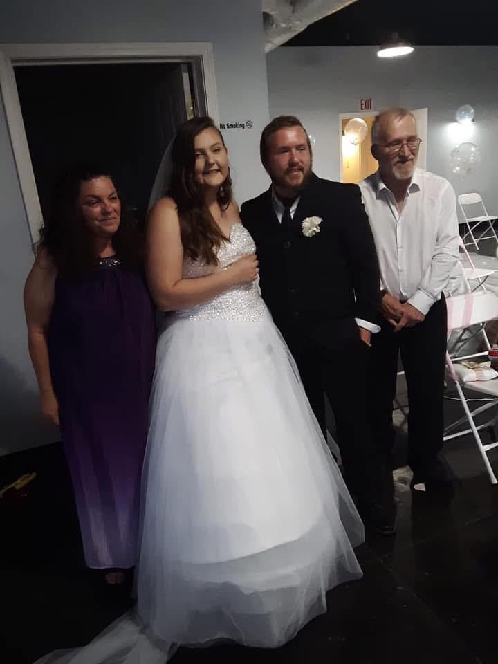 Four people stand together at a wedding. A bride wears a white dress and smiles.