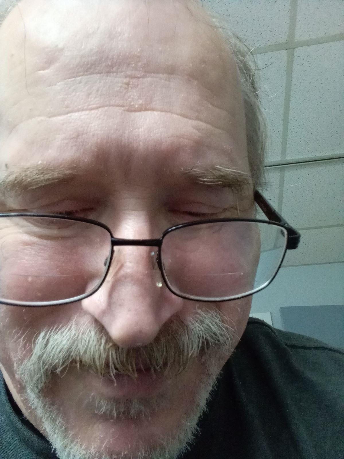 Man sits indoors with closed eyes and a smile, enjoying a moment of happiness.