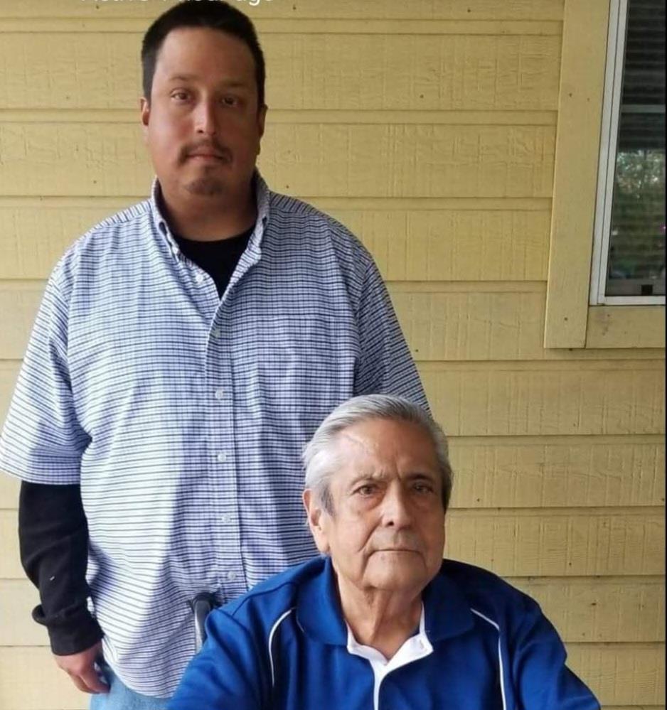 Two men are standing in a garden near a wooden wall while spending time together outside.