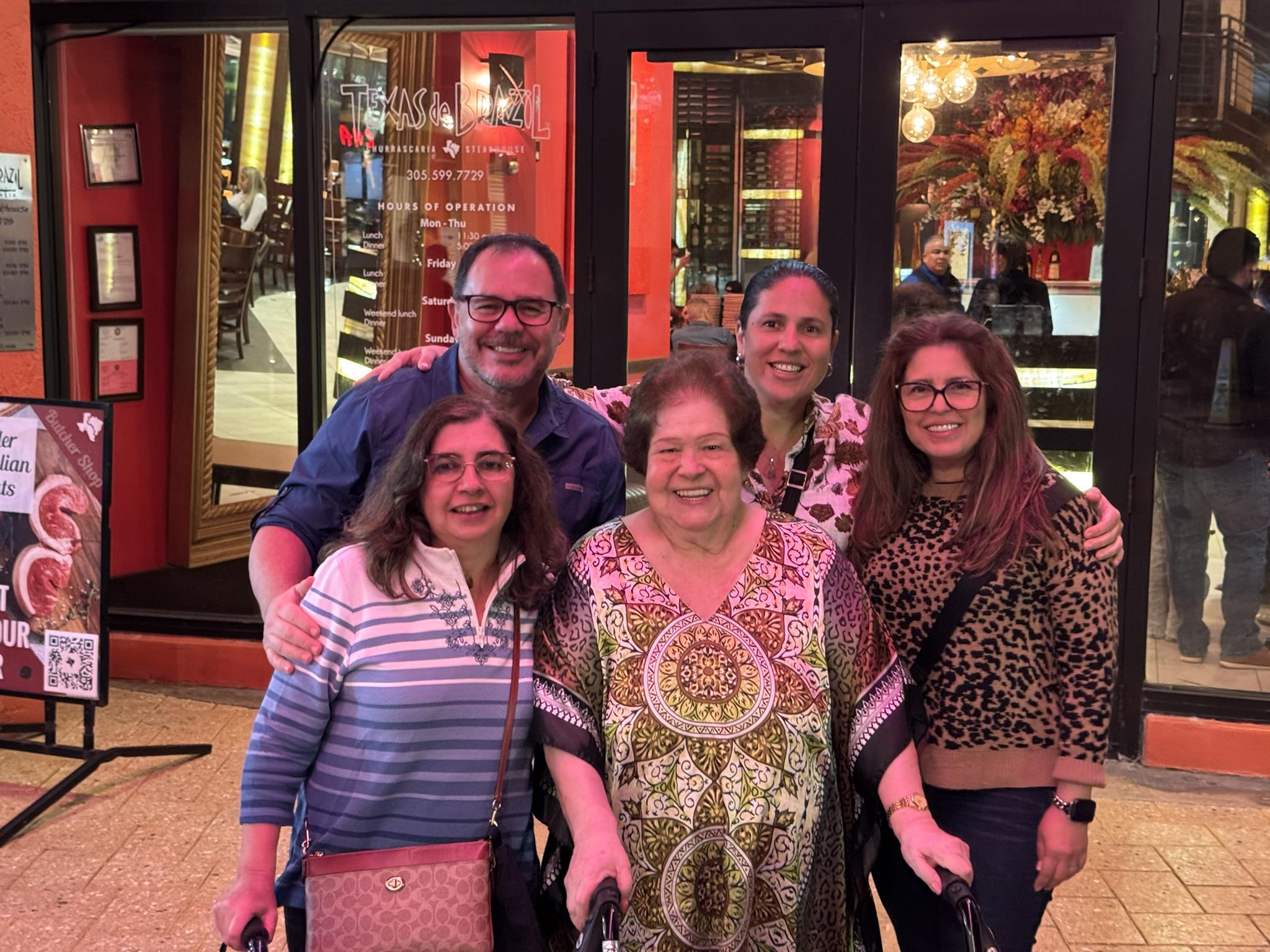 Group of five people stand close together outside a restaurant while smiling for a picture.