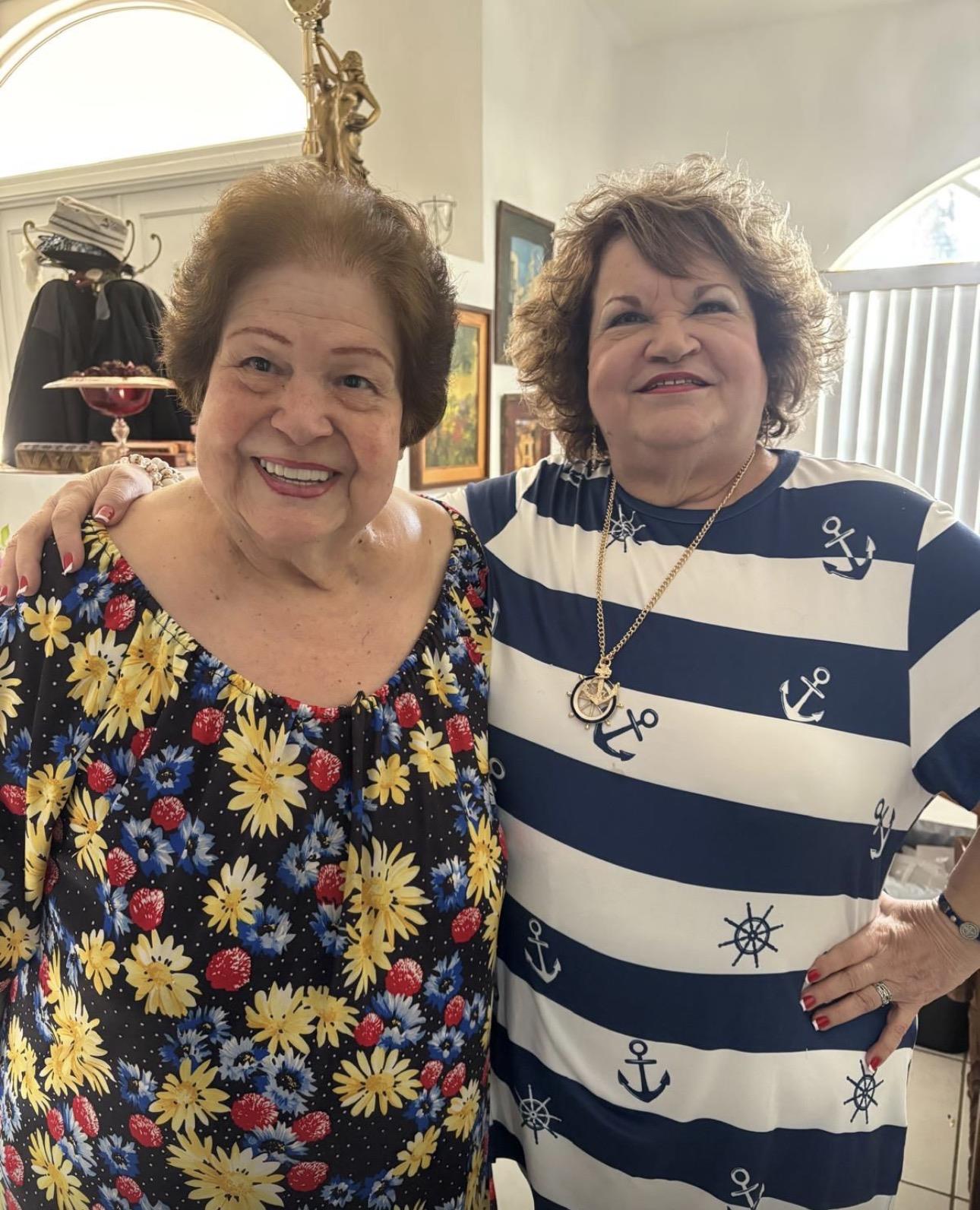 Two friends smile widely while standing close together in a home setting during the afternoon.