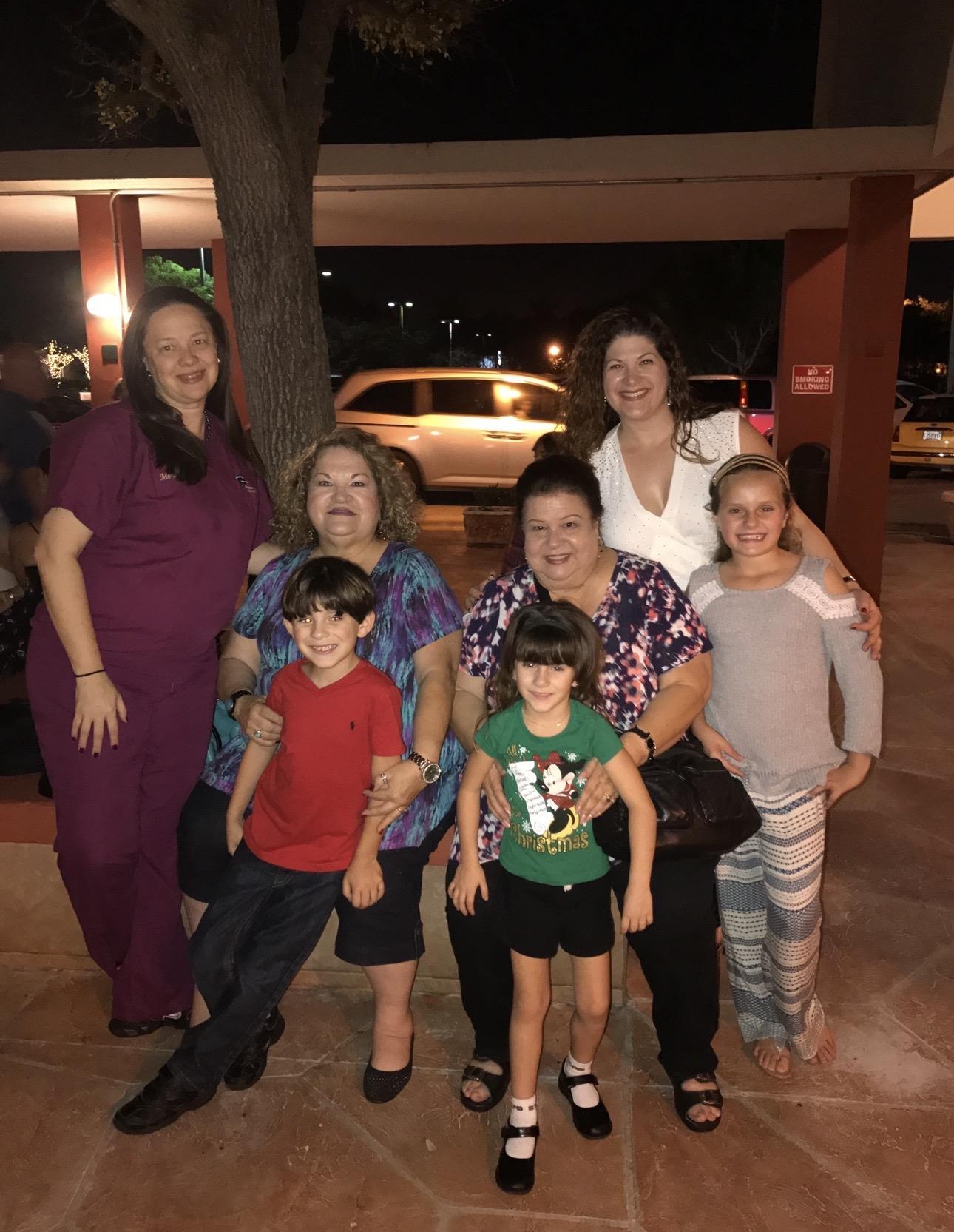 A group of four women and three children stand together outside a building at night.
