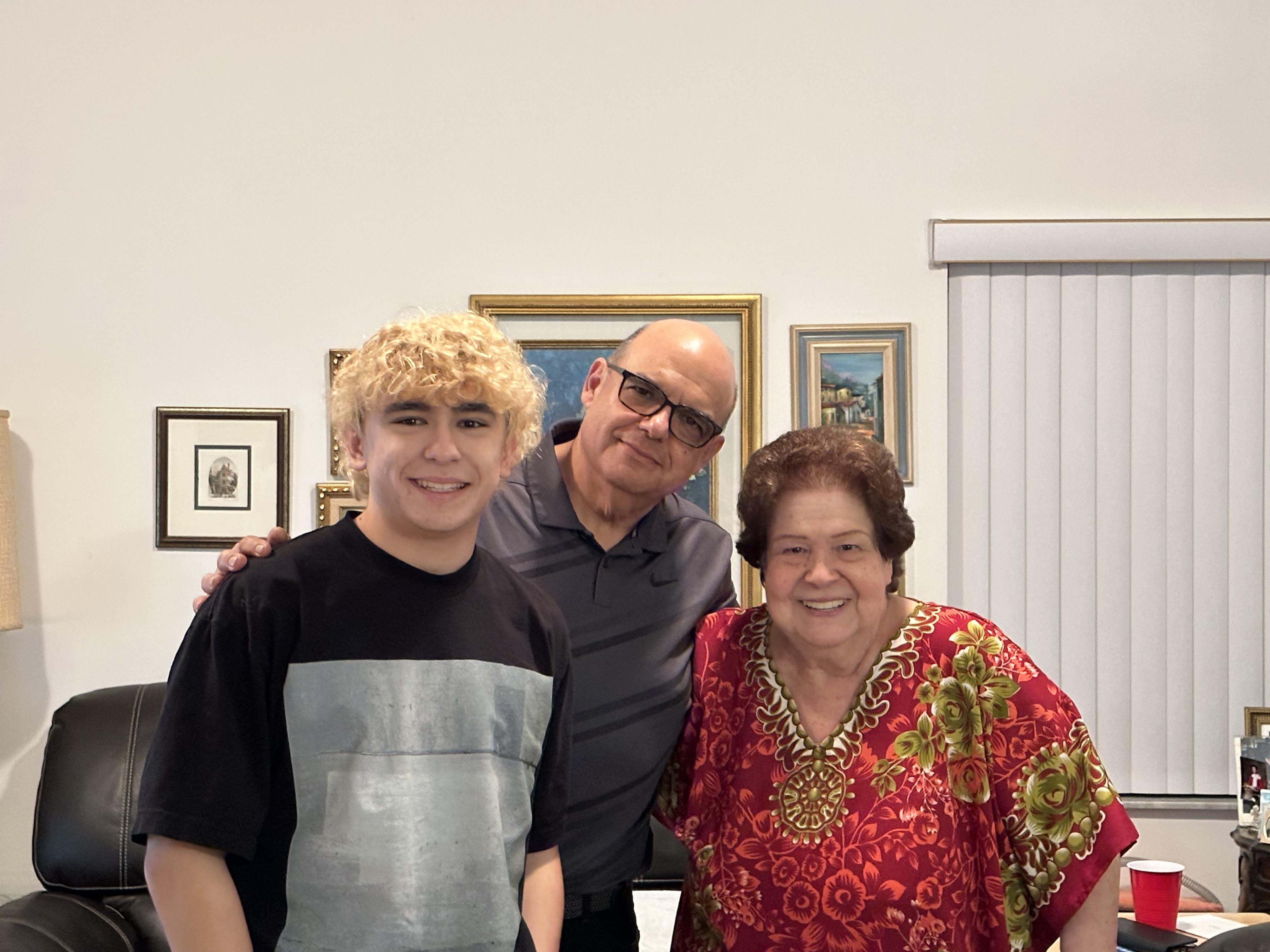 Three people pose for a picture in a living room with art on the walls.