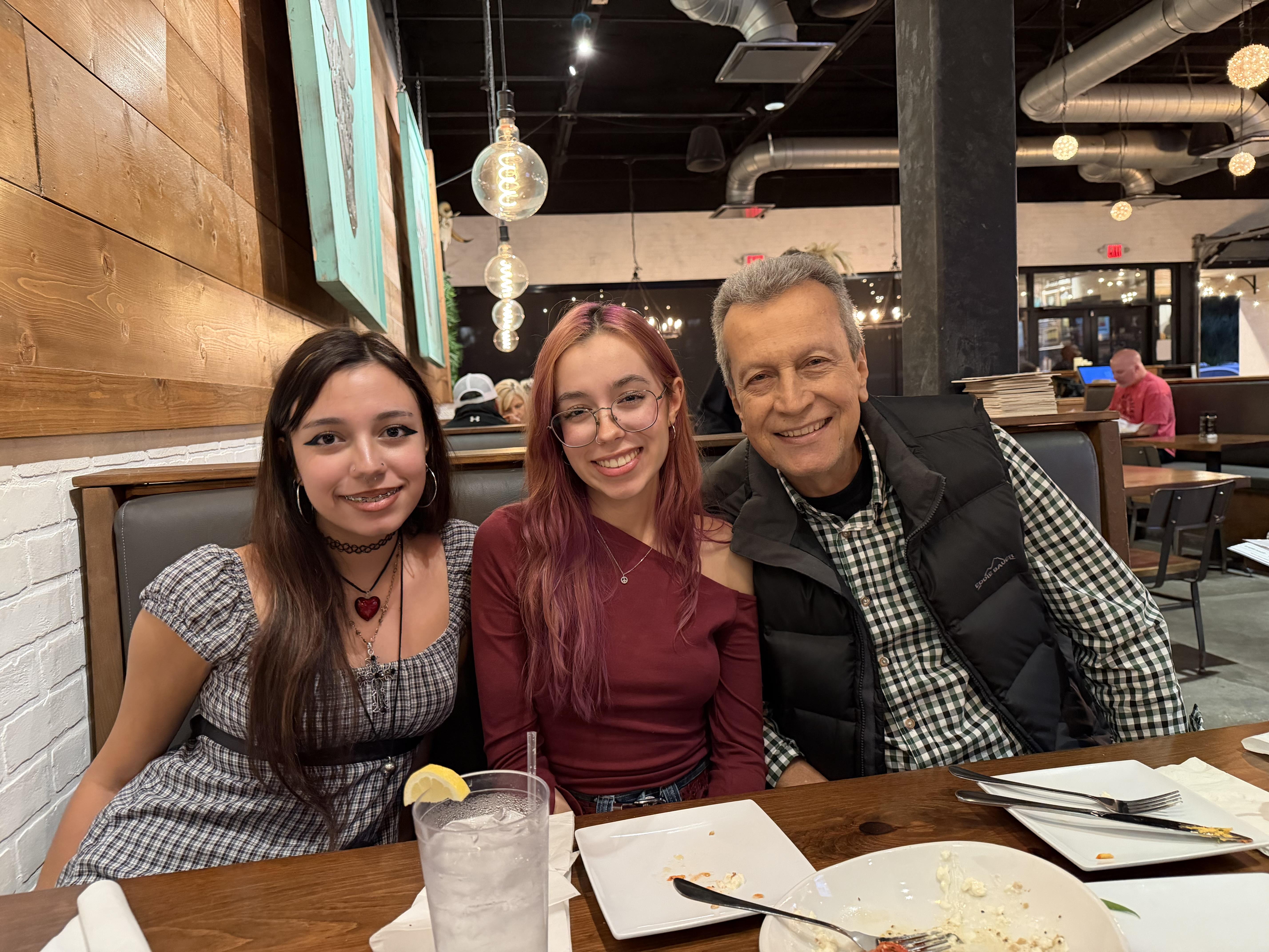 Two young women and an older man sit at a table in a restaurant.