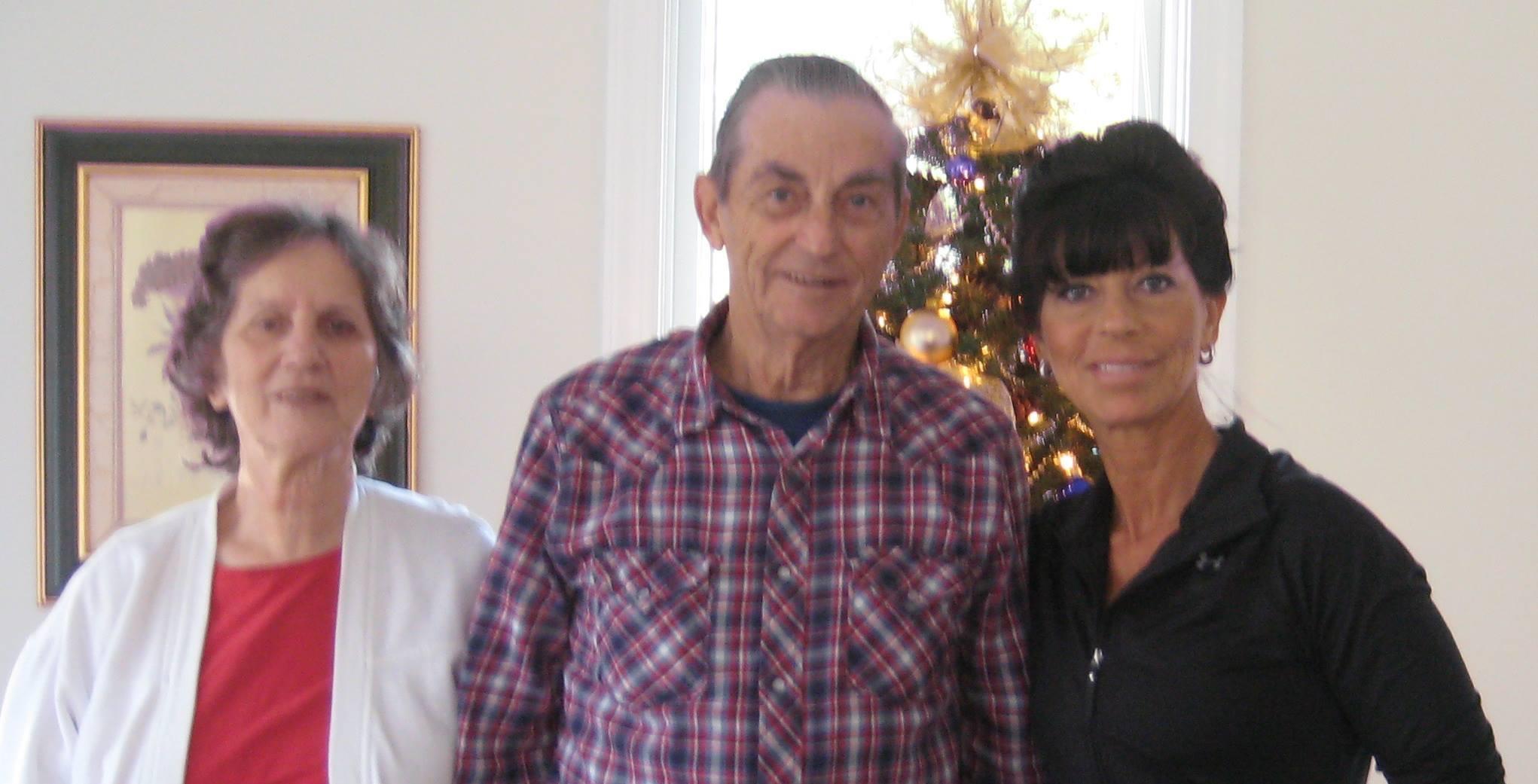 Three friends stand together in a room with holiday decorations and a Christmas tree behind them.