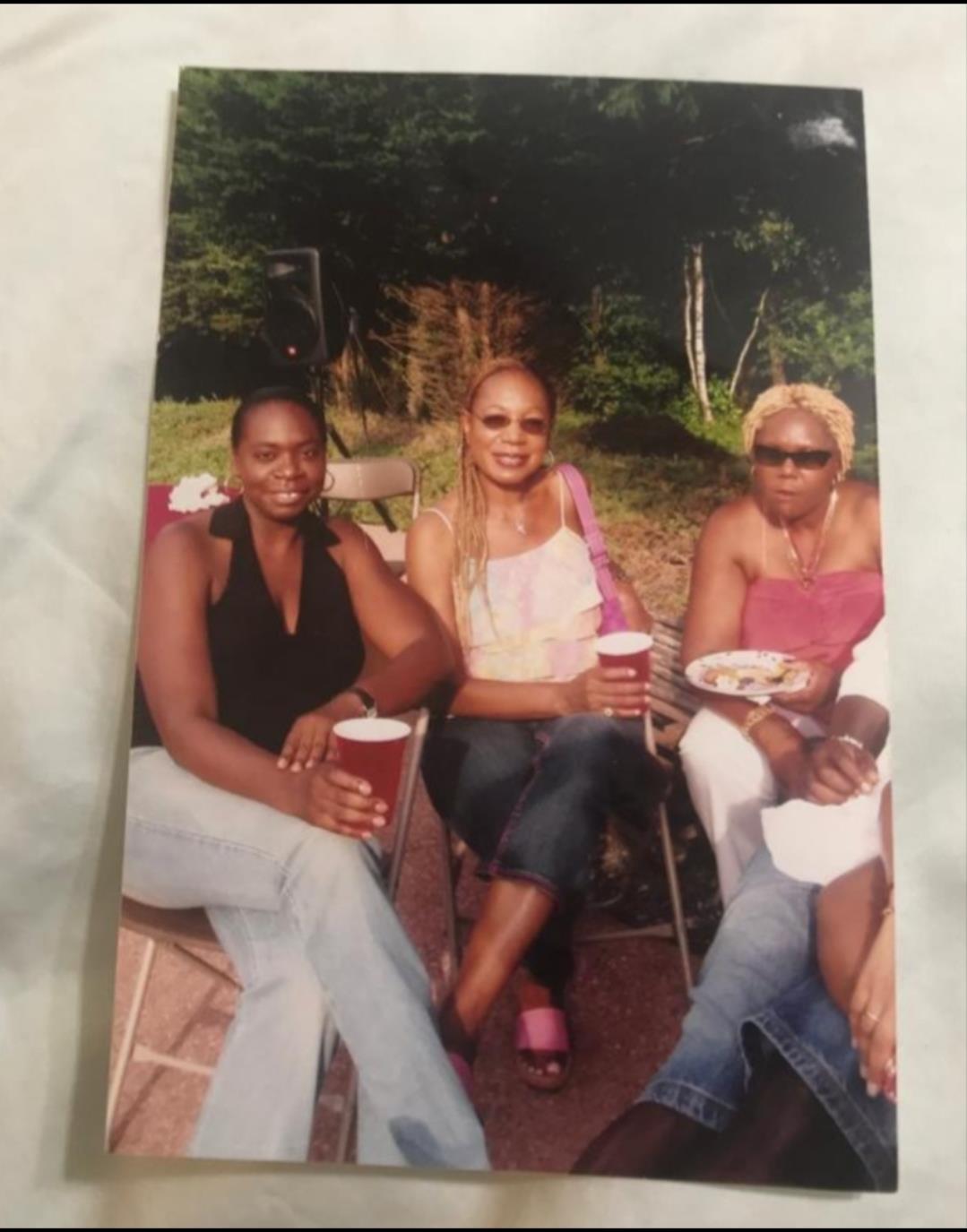 Three friends sit together outdoors, each holding a drink and sharing moments of laughter.