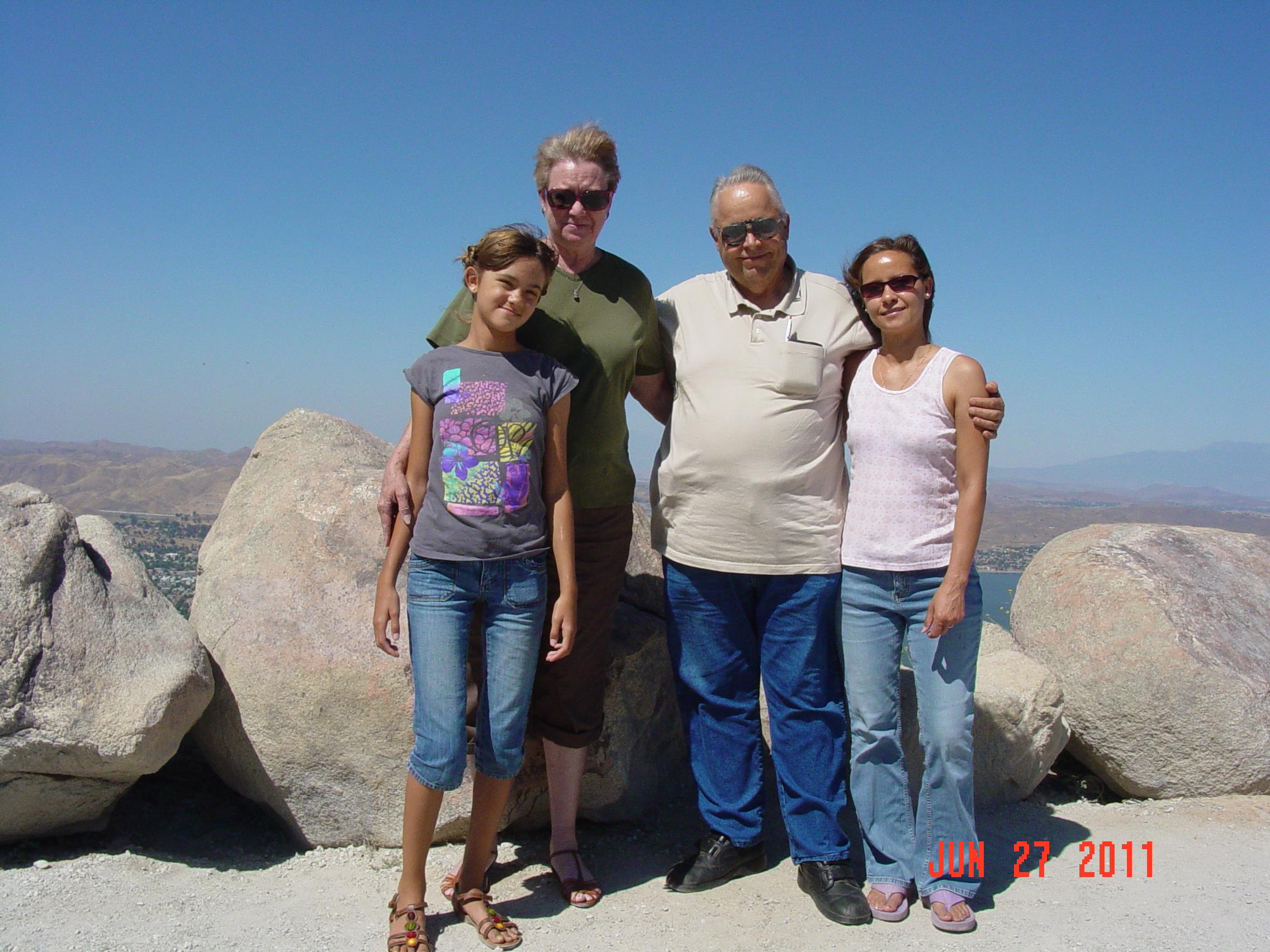 Four family members pose for a picture on a rocky surface with a blue sky above.