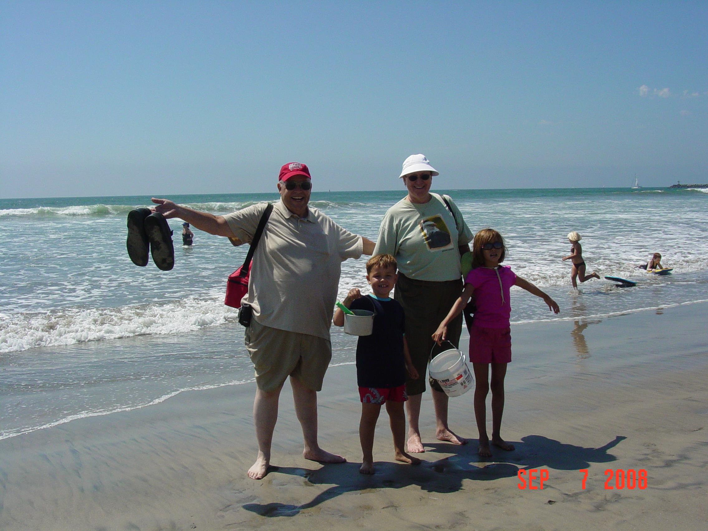 Group of four stands by the water at the beach. Children play in the ocean waves.