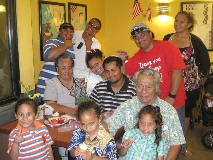 Adults and children gather at a table, sharing food and drinks while smiling.