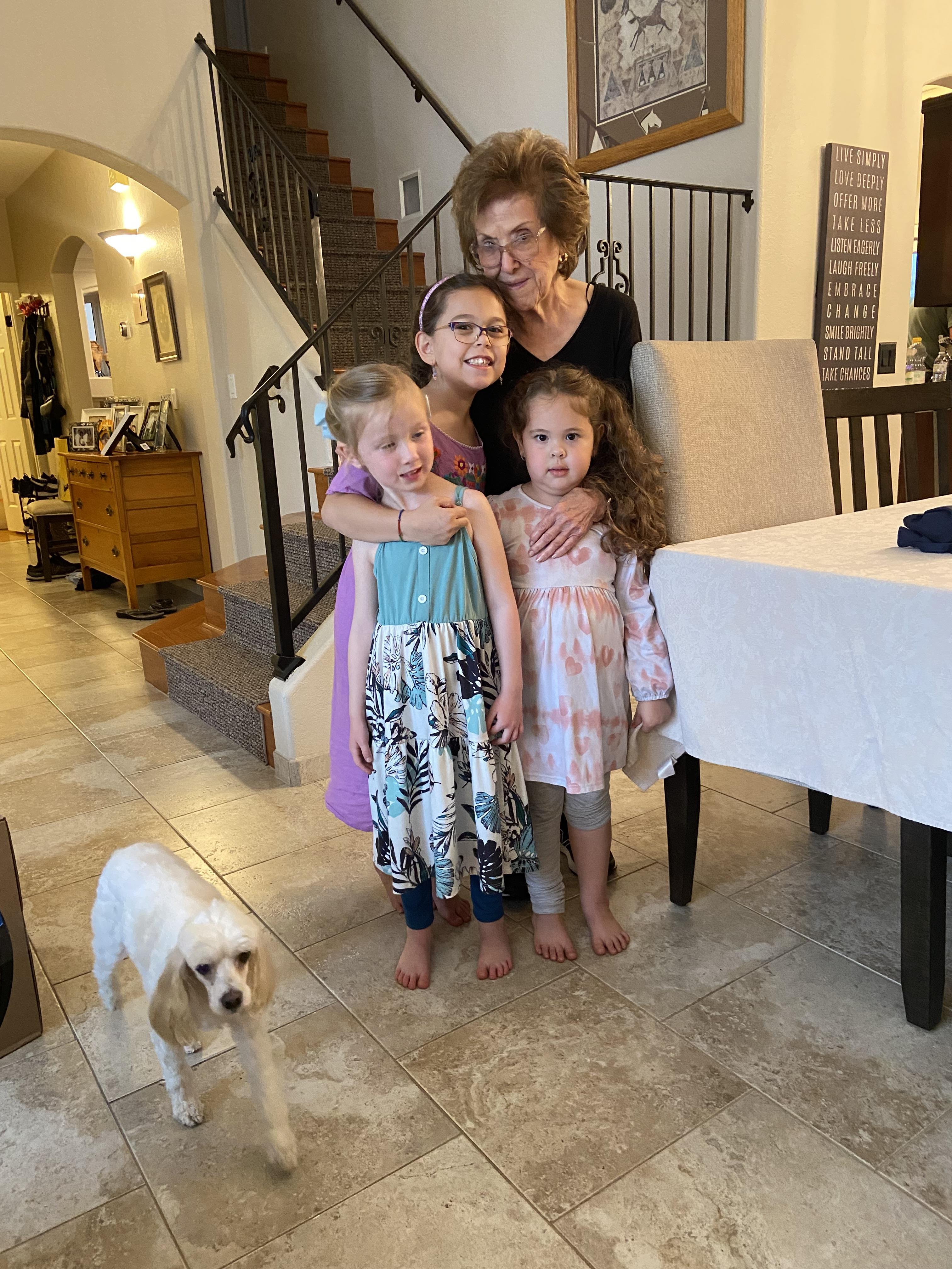 A group of four people stands together in a living room. Two children and an adult smile.