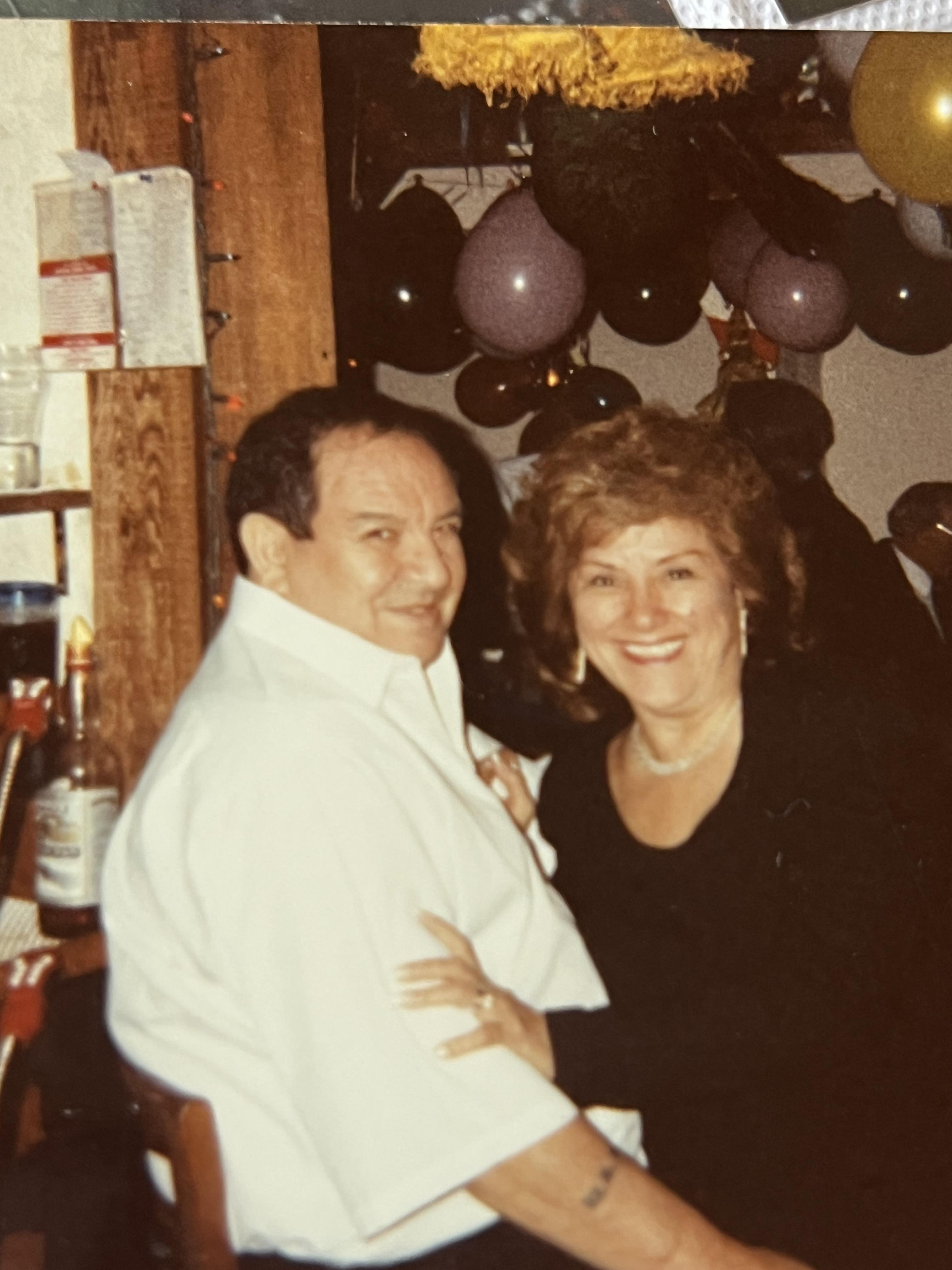 A couple enjoys dancing at a party in a bar with balloons in the background.