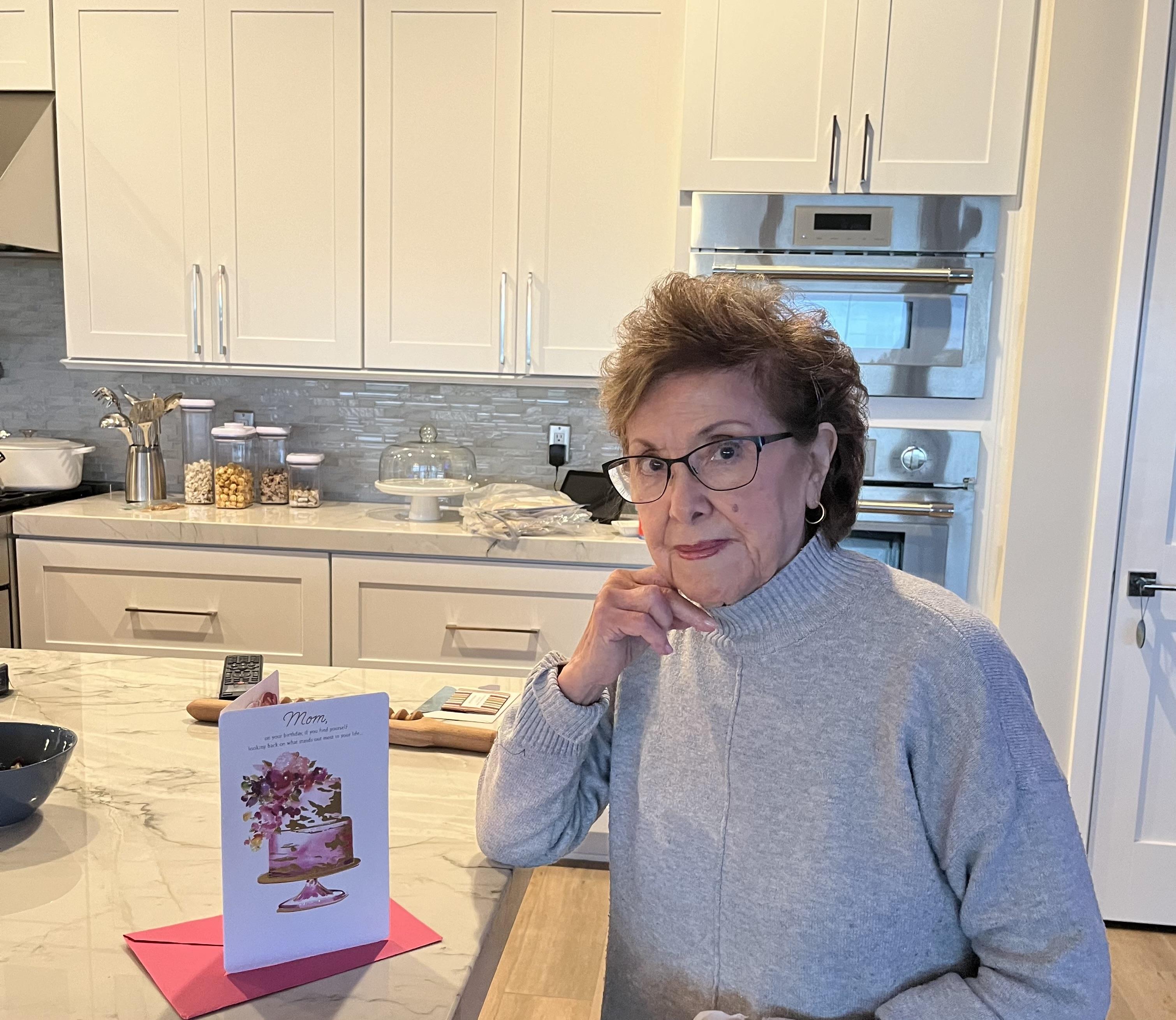 A woman is sitting at a kitchen counter with a birthday card in front of her.