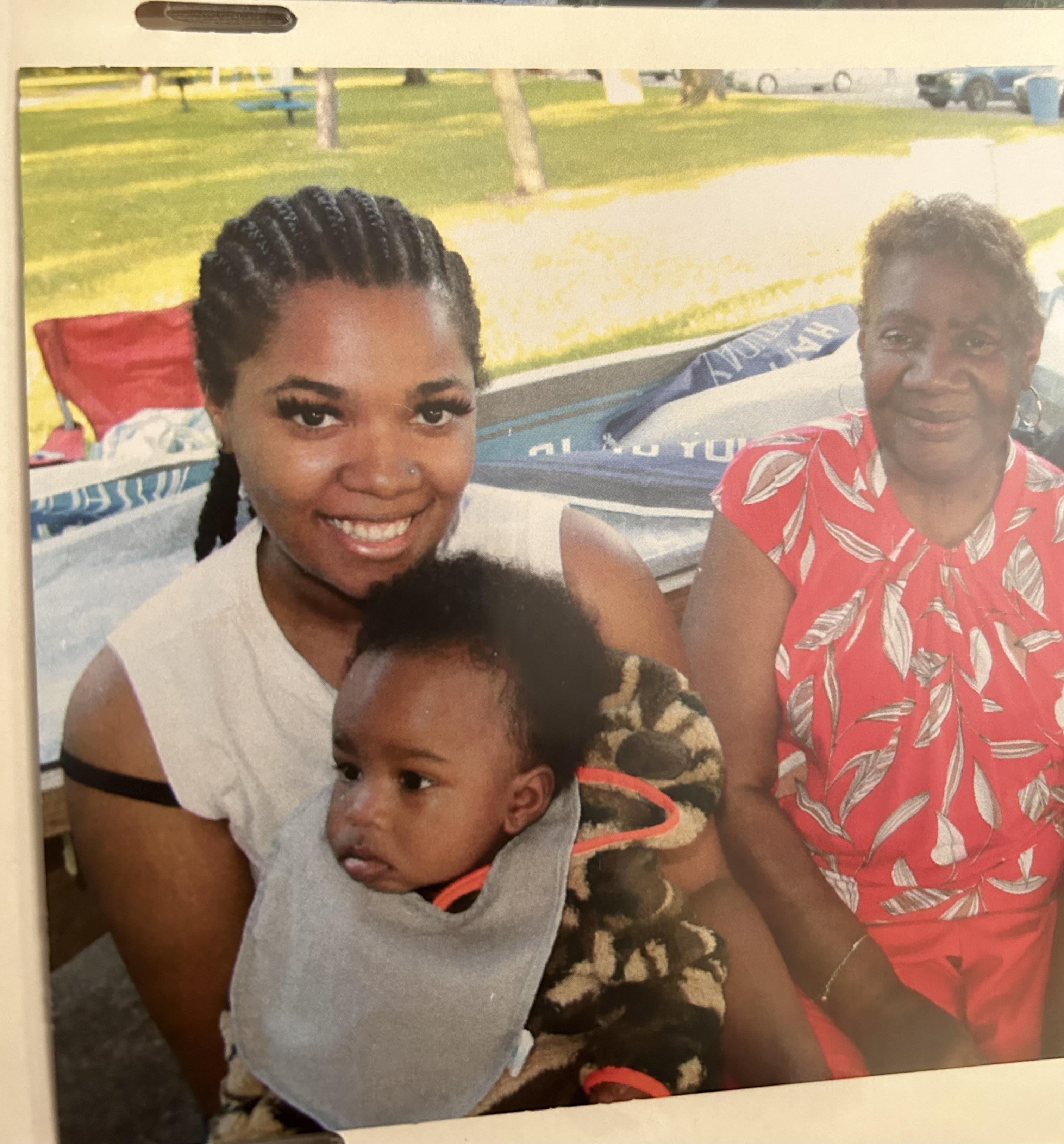 A woman holding a baby and a woman sitting on a bench