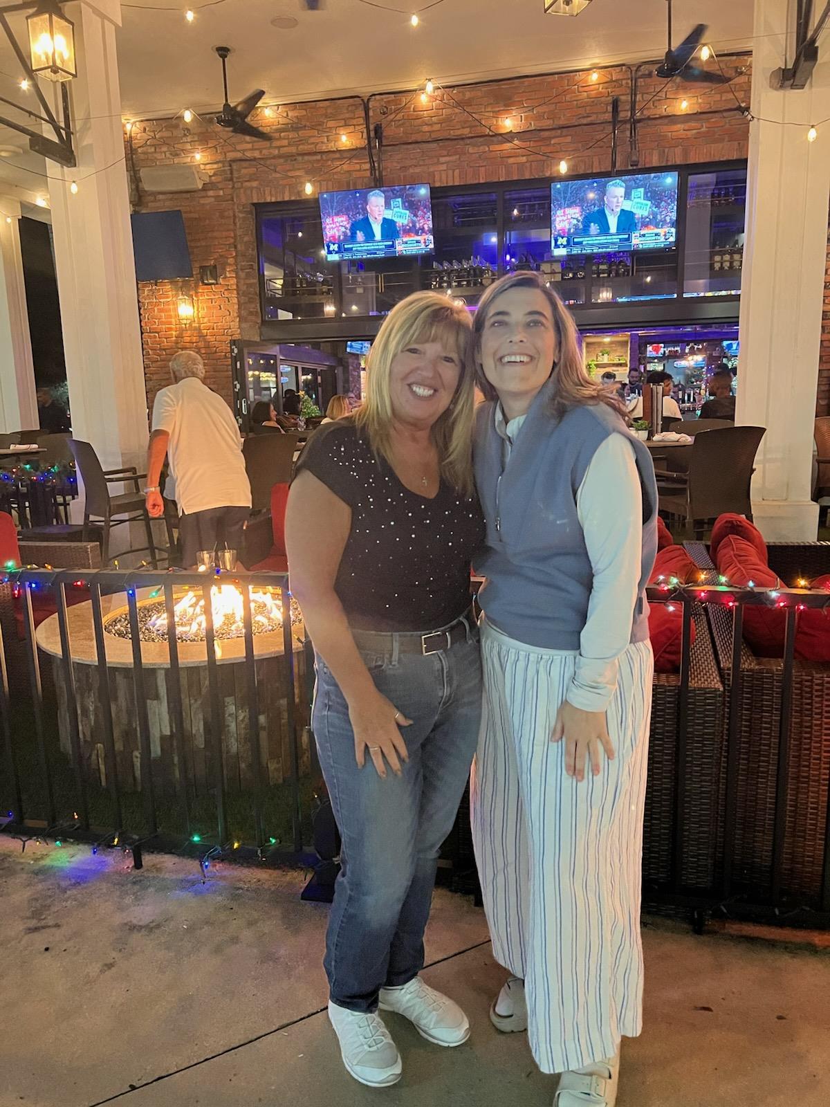 Two women standing together in front of a bar