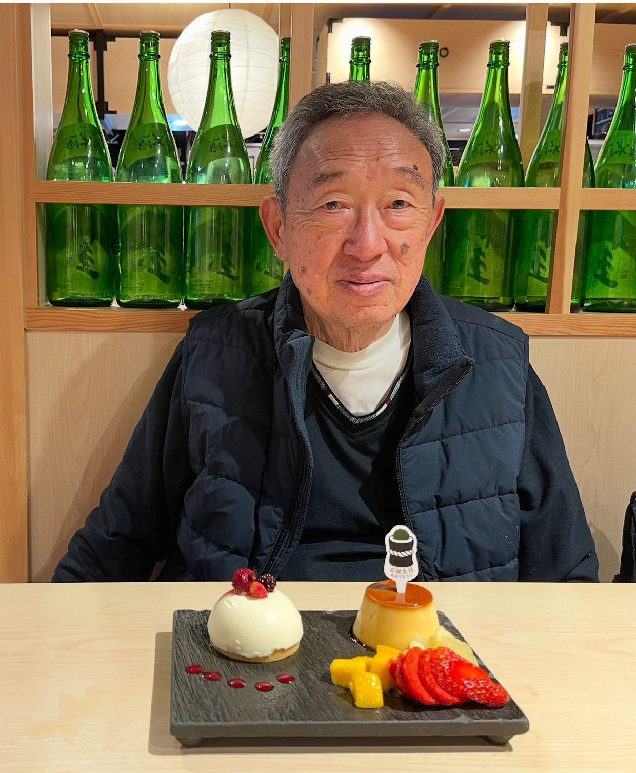 An elderly man savors desserts at a restaurant with drinks in the background.