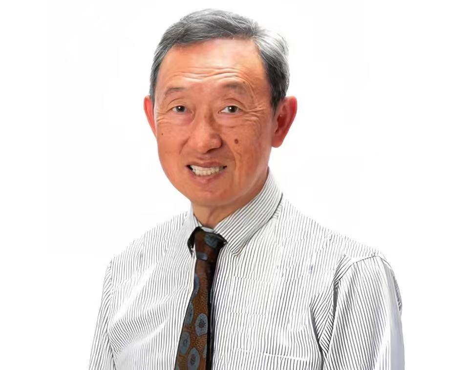 A man stands and smiles while wearing a striped shirt and a tie in a simple setting.