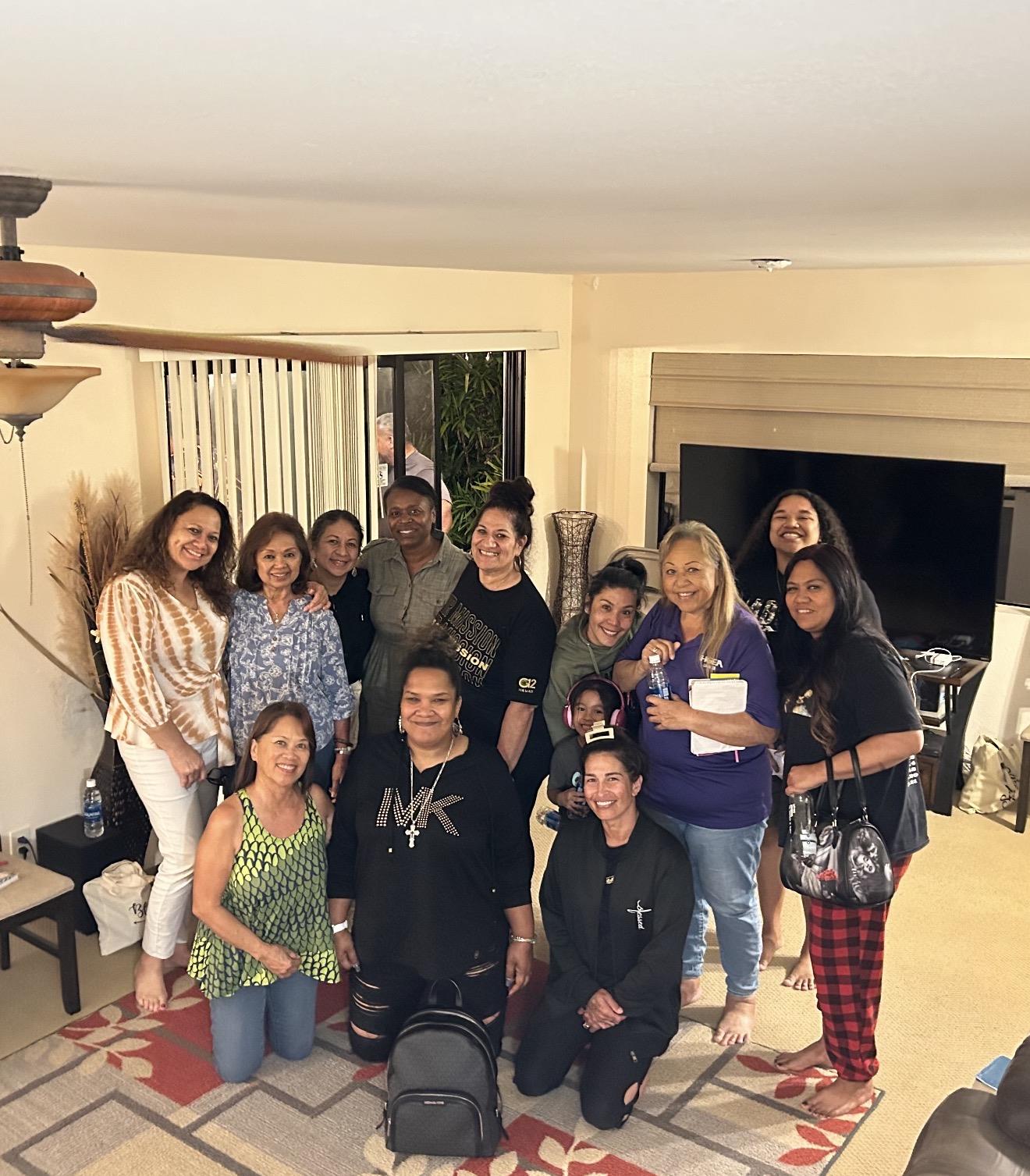 Women stand and sit together in a living room during a gathering filled with joy and conversation.