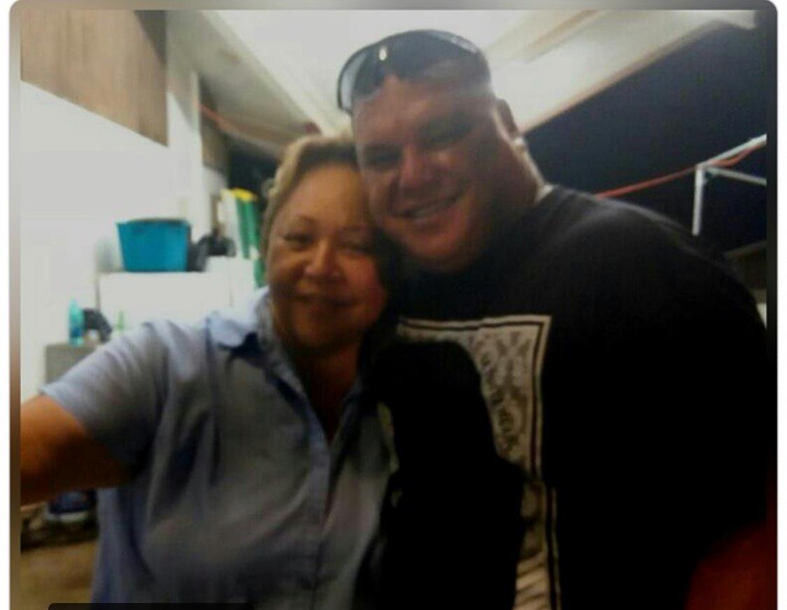 Two individuals stand close together and smile for a picture in a relaxed indoor setting.