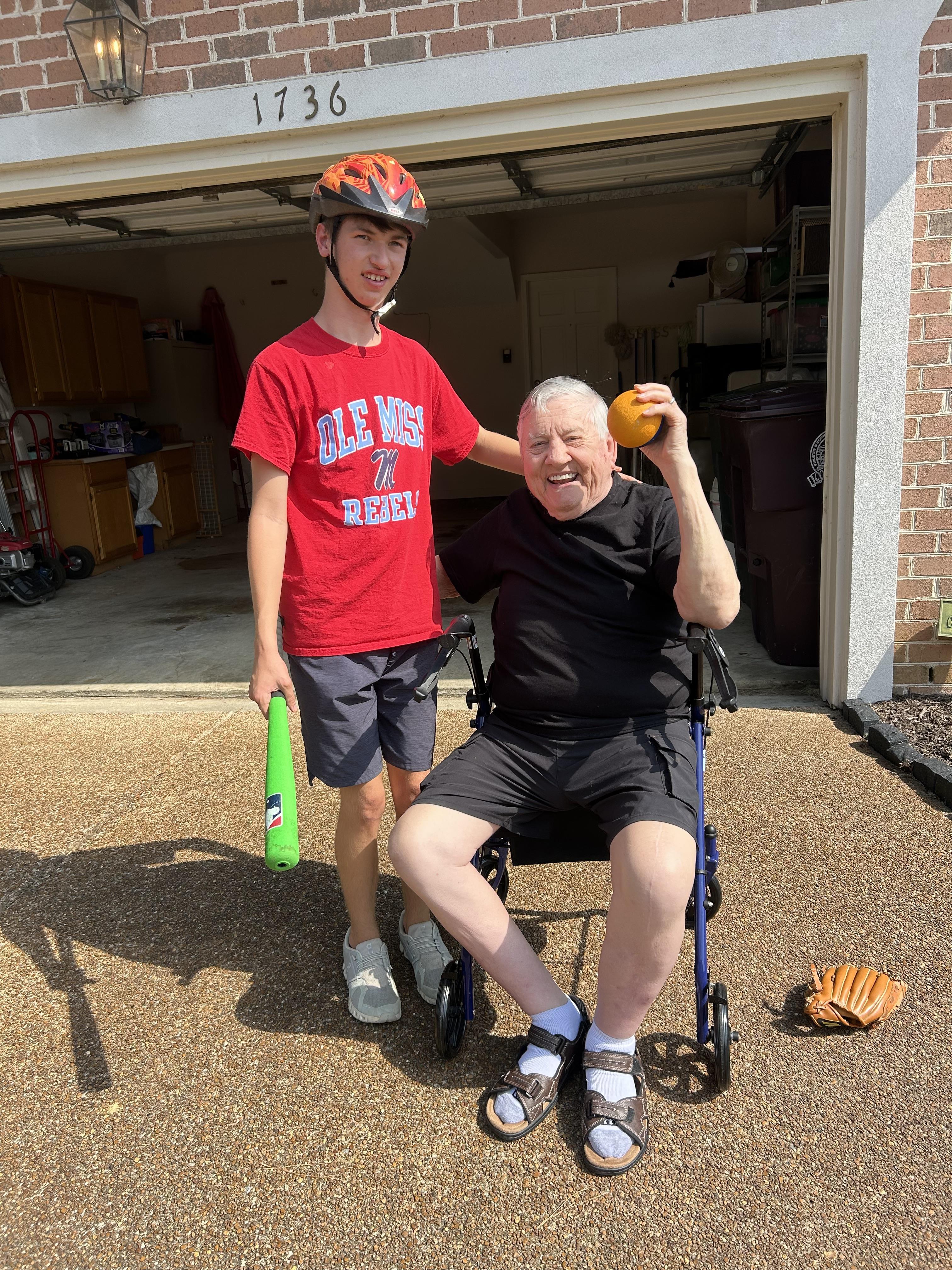 A man in a wheelchair enjoys a baseball with a young man standing nearby.