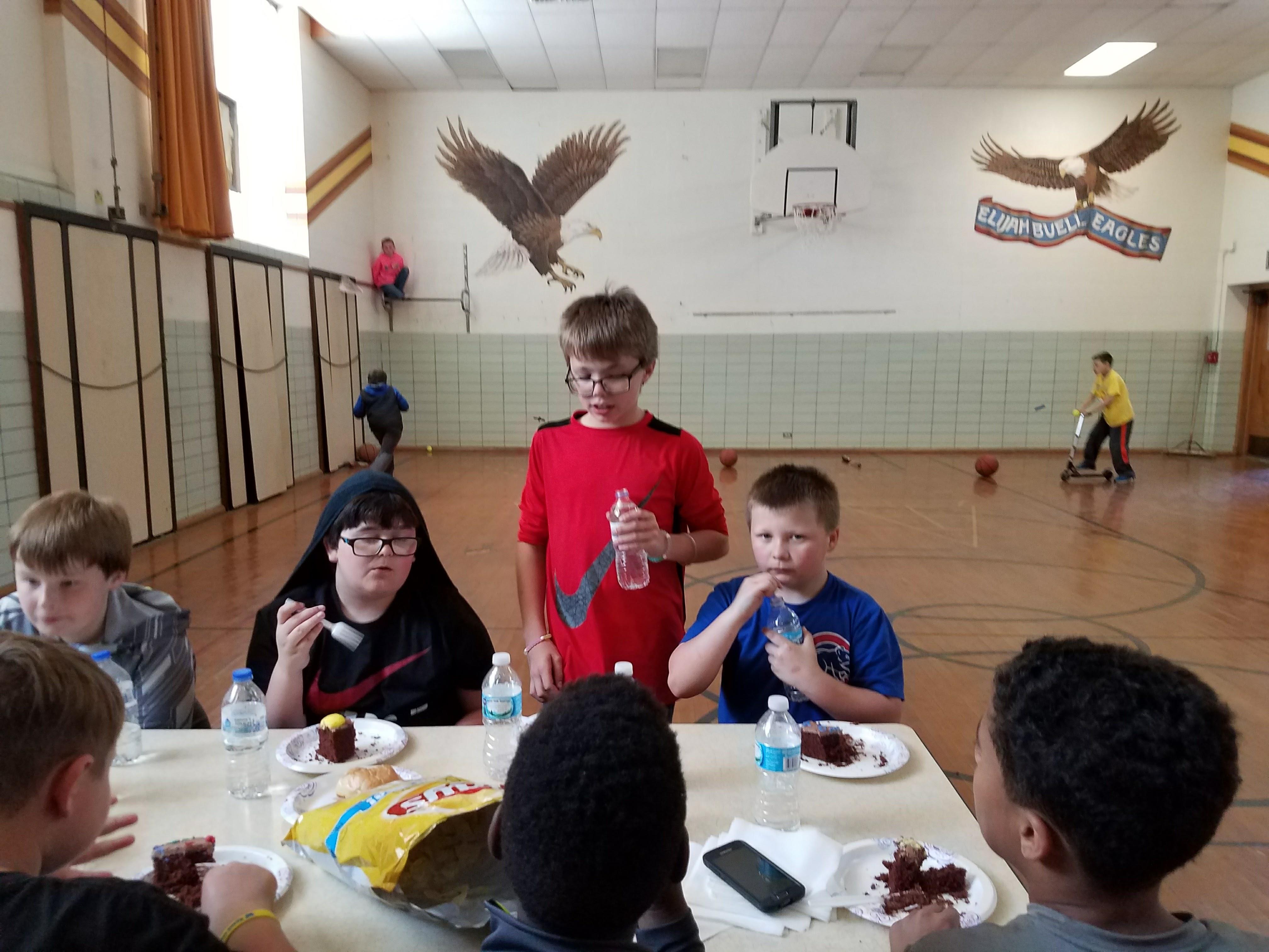 A group of kids sitting at a table with food and water bottles