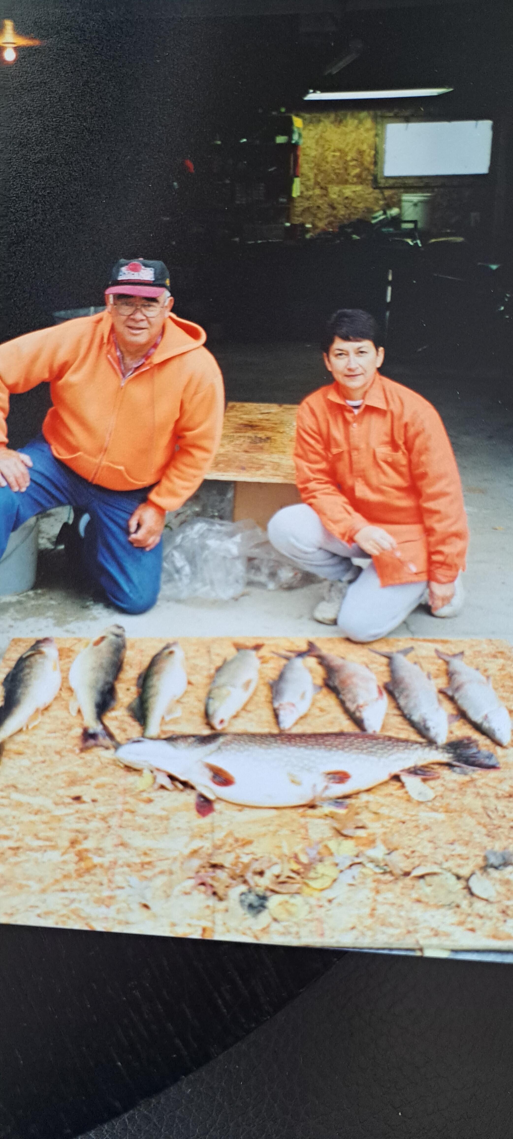 A couple of men kneeling next to a pile of fish