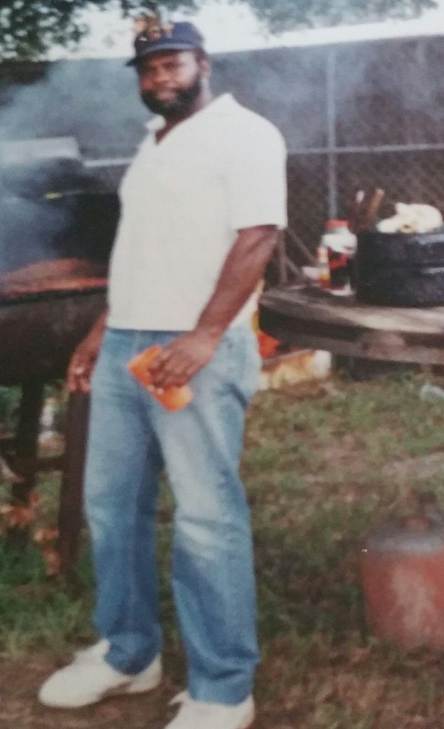 A man stands beside a cow on a farm. He holds an orange object in his right hand.