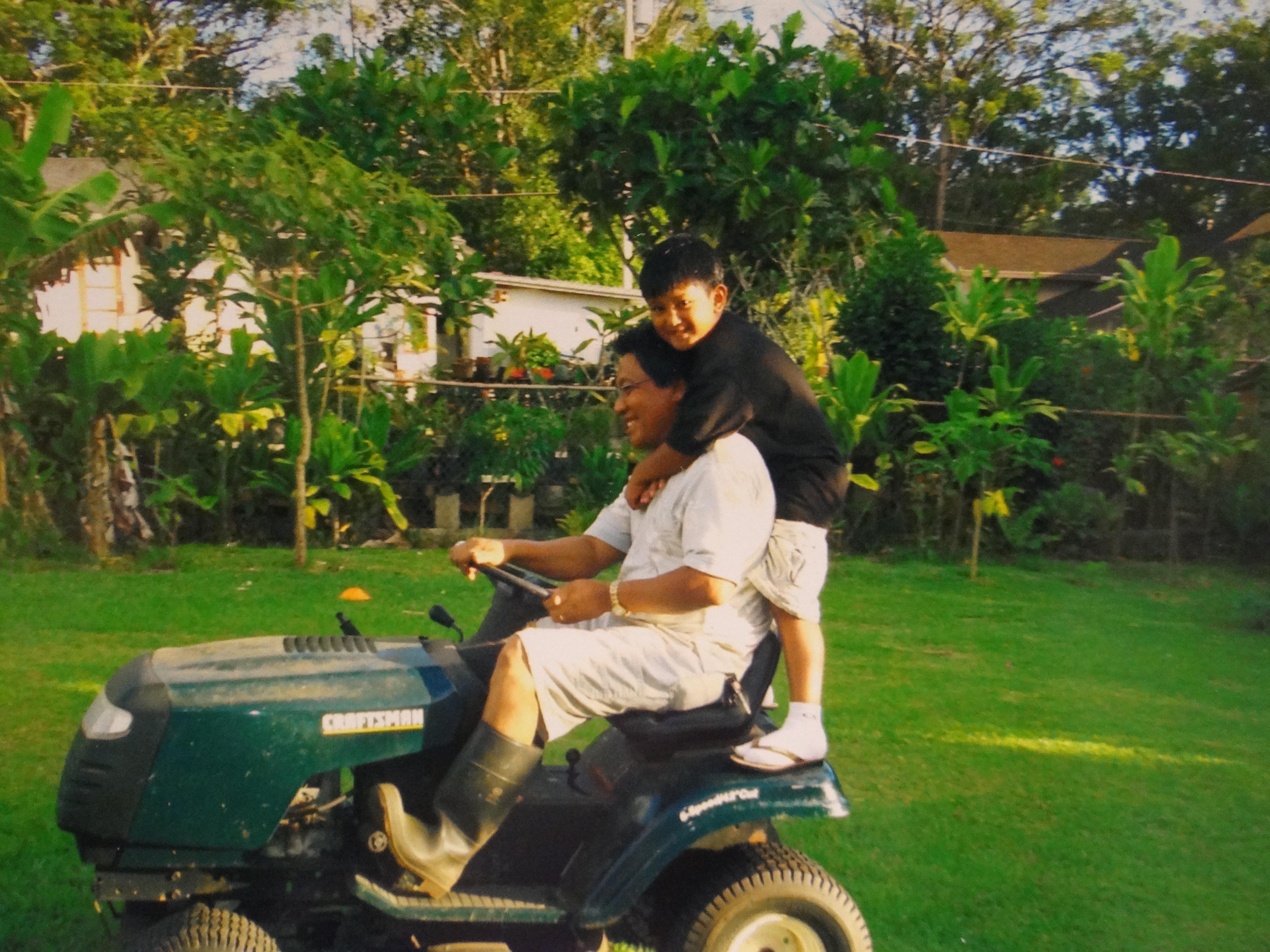 A man and boy riding a lawnmower