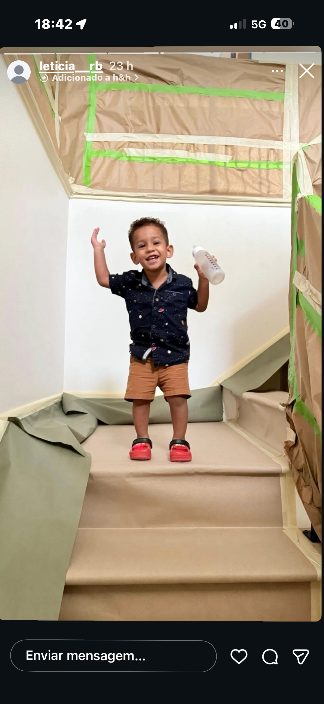 A young child smiles and raises hands while standing on stairs with a bottle.