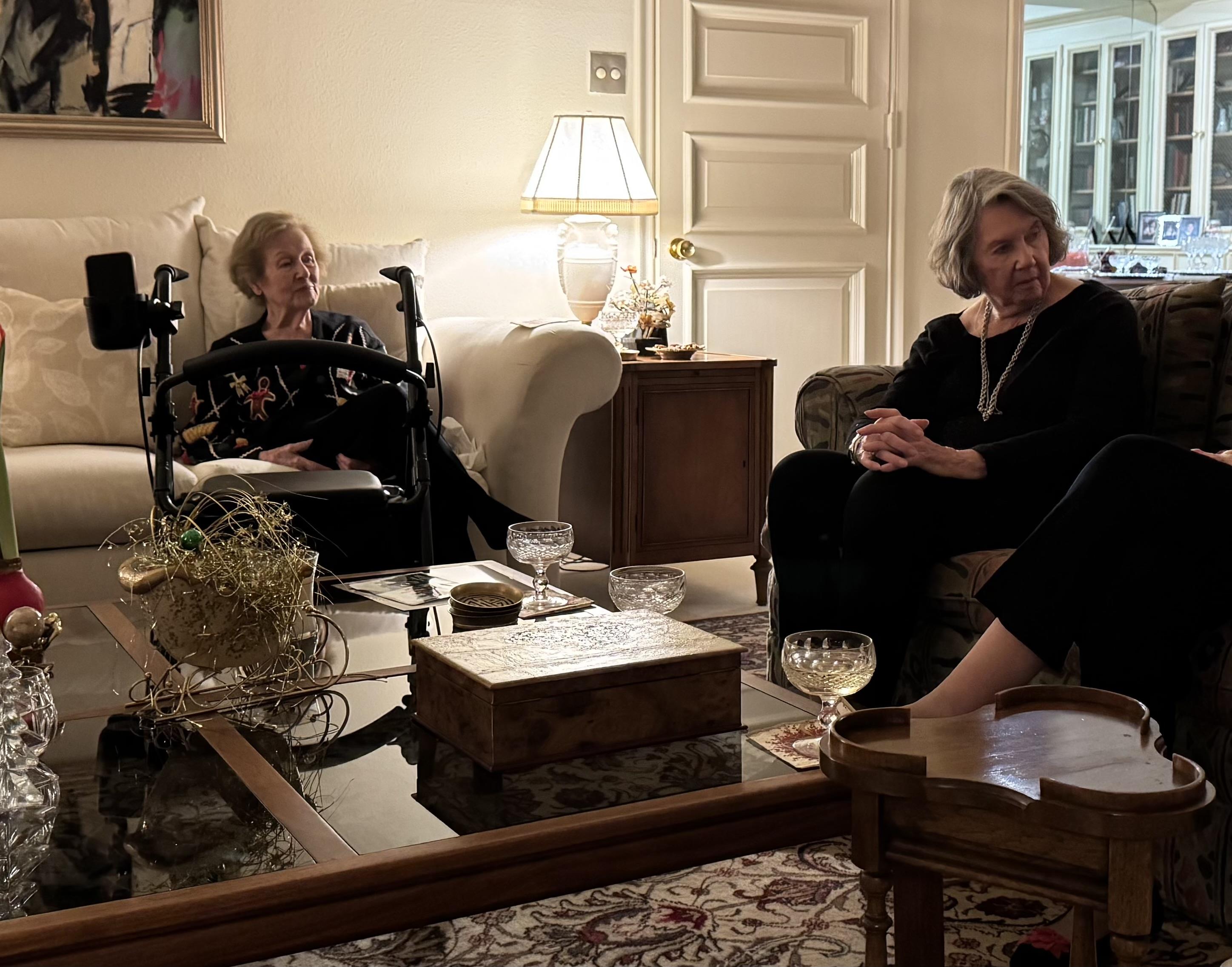Three friends sit together in a living room sharing stories and enjoying drinks at night.