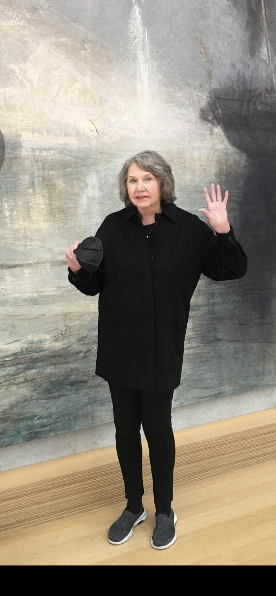 A woman gestures with her hand while holding a dark object in an art gallery.
