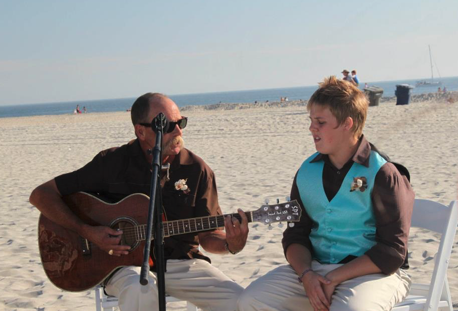 A man and boy playing guitar on a beach