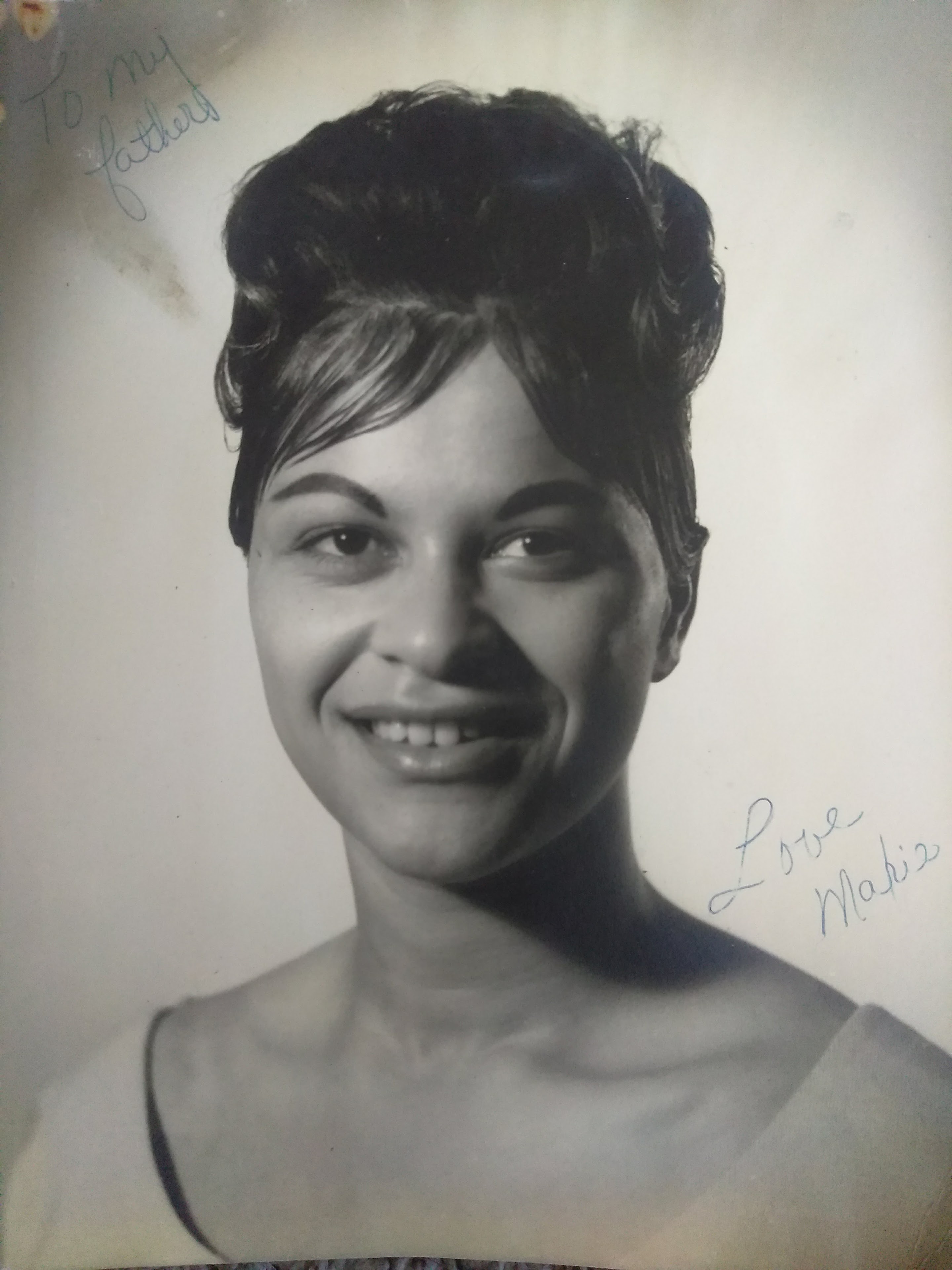A woman stands with a bright smile in a black and white setting, showcasing her hairstyle.
