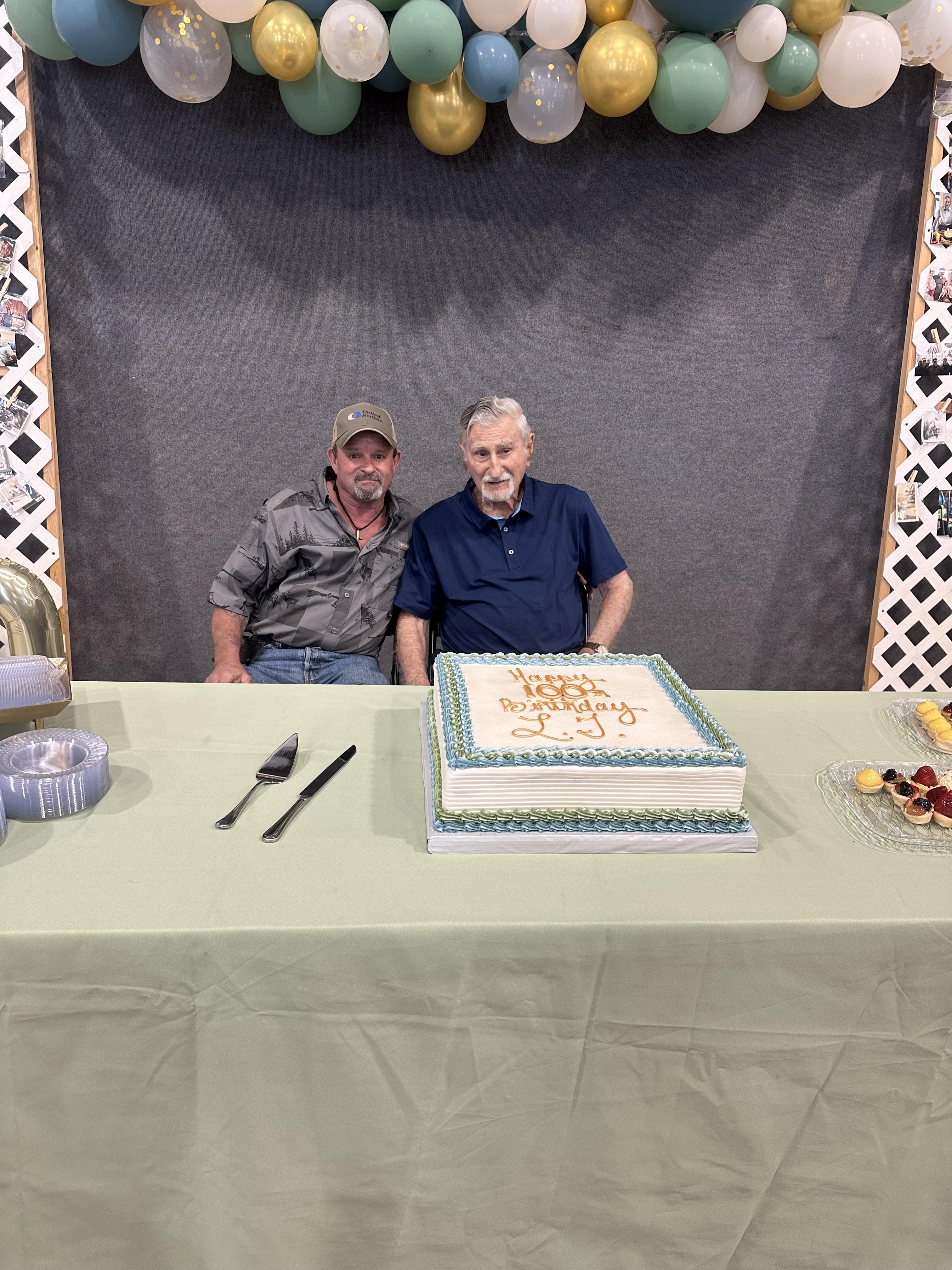 Two men sitting at a table with a cake