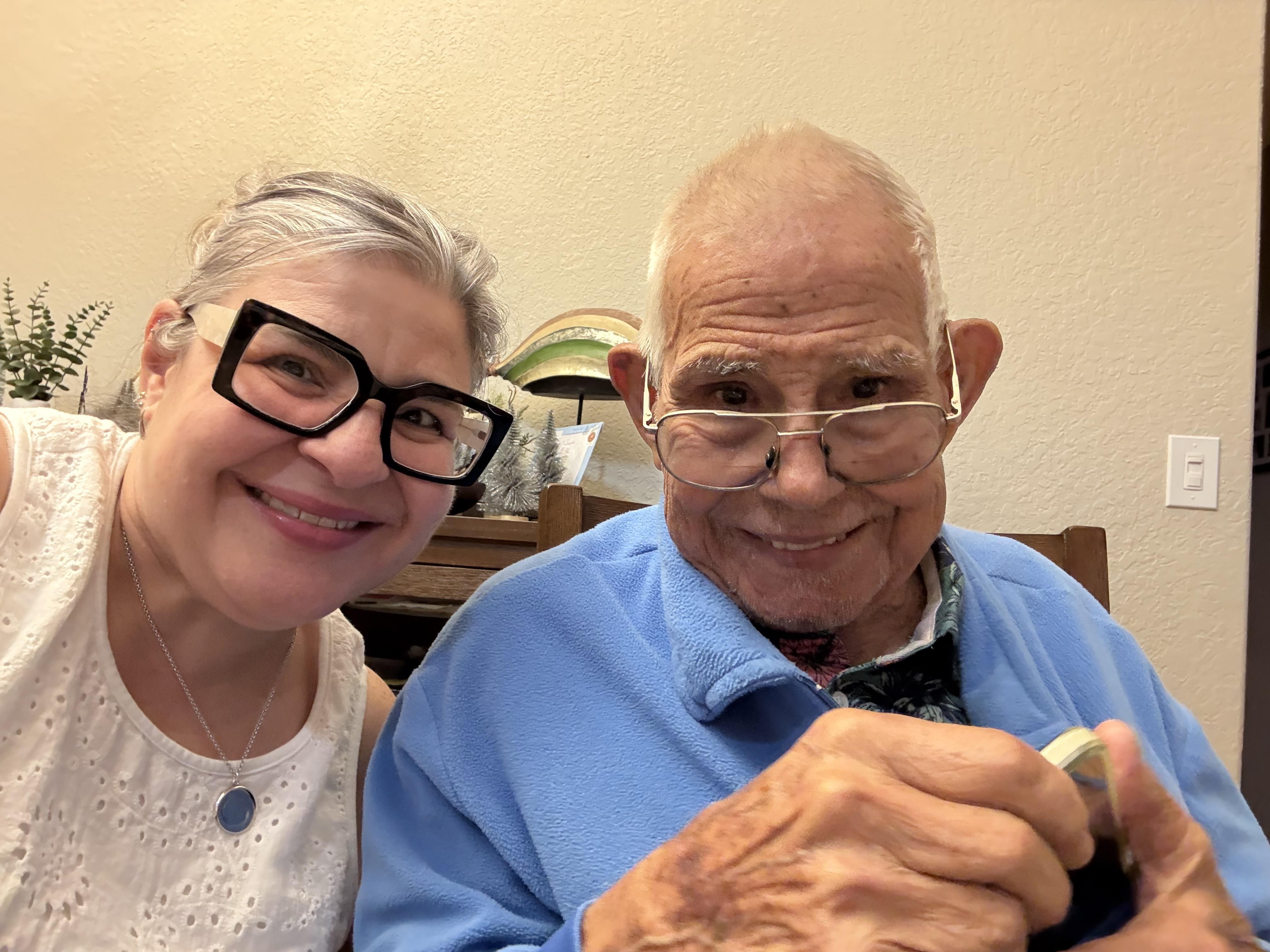 A woman and an elderly man share smiles and conversation in a warm indoor space.